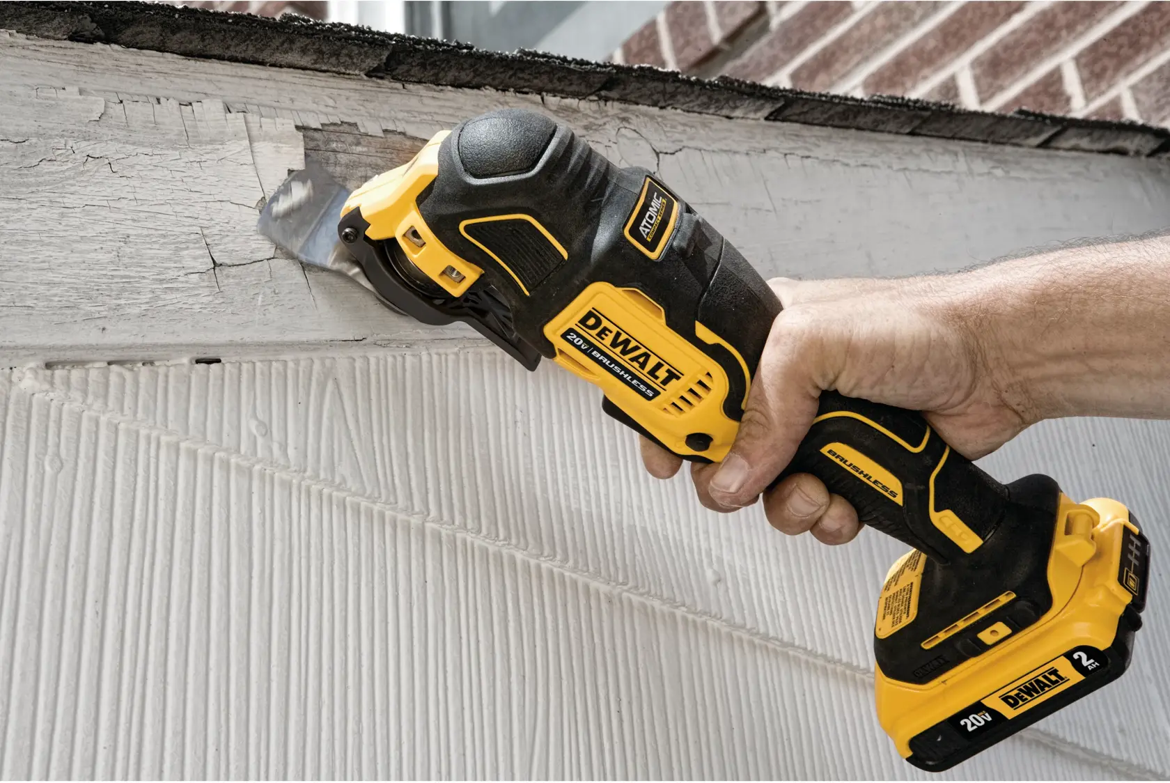 A person using a DEWALT DCS354B cordless oscillating multi-tool to cut or remove material from a wooden surface near a house exterior.