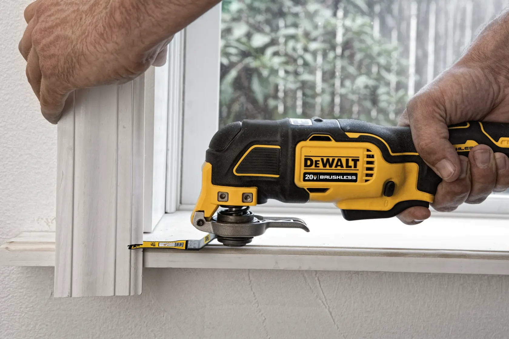 A person uses a DEWALT 20V brushless oscillating multi-tool to cut molding near a window.