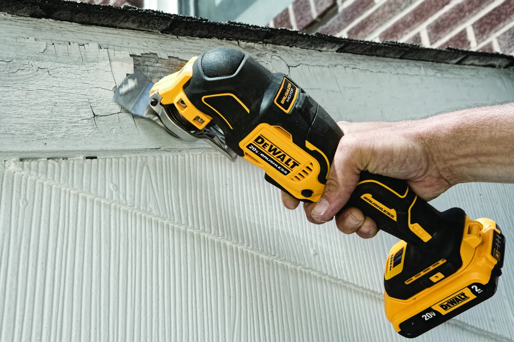 A person uses a DEWALT cordless oscillating multi-tool to scrape paint from a wooden surface.