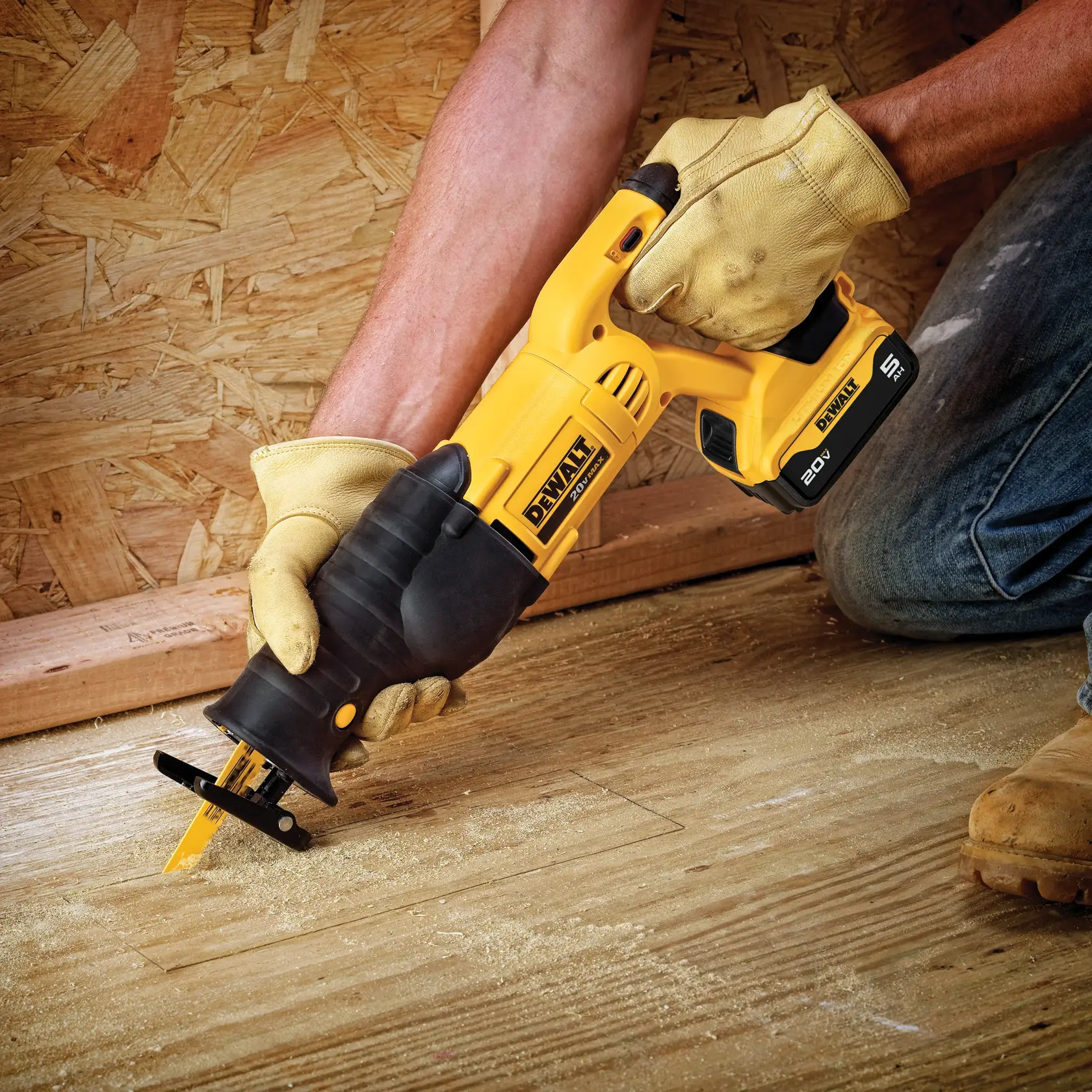 A person wearing work gloves uses a DEWALT 20V cordless reciprocating saw to cut wood flooring in a construction setting.