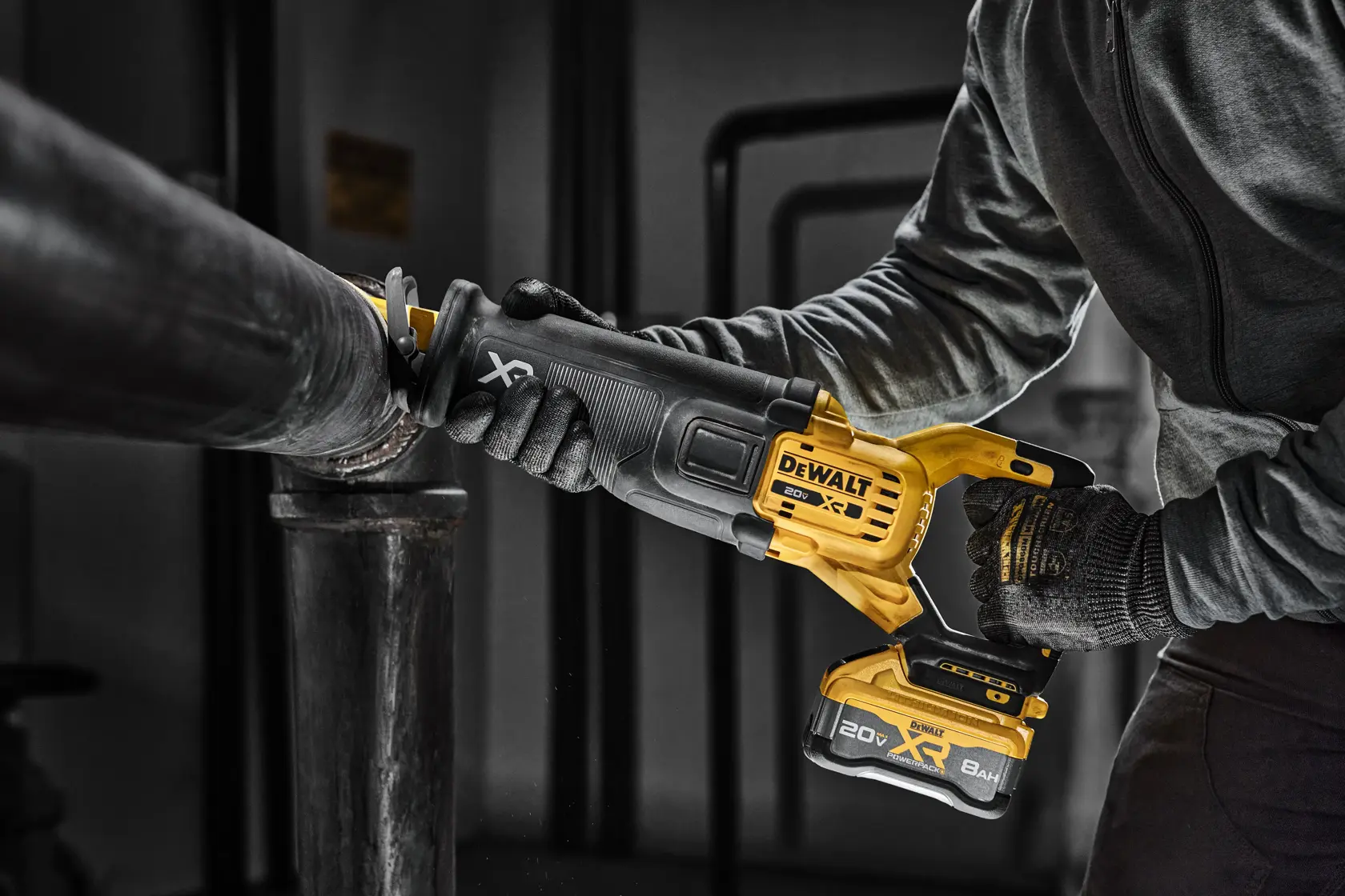 A person using a DEWALT cordless reciprocating saw to cut through a metal pipe. The tool has a yellow and black design and is powered by a 20V XR battery.