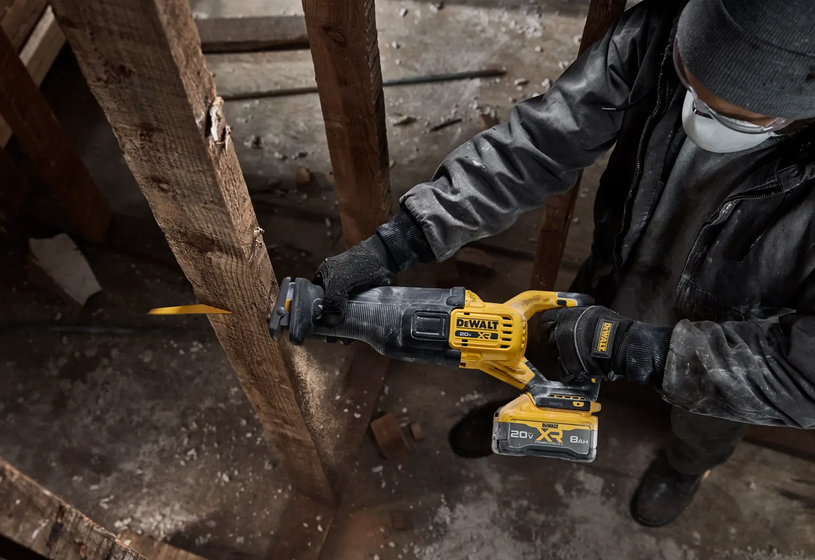 A person wearing gloves and a mask is using a DEWALT 20V cordless reciprocating saw to cut through a wooden beam in a construction or renovation setting.