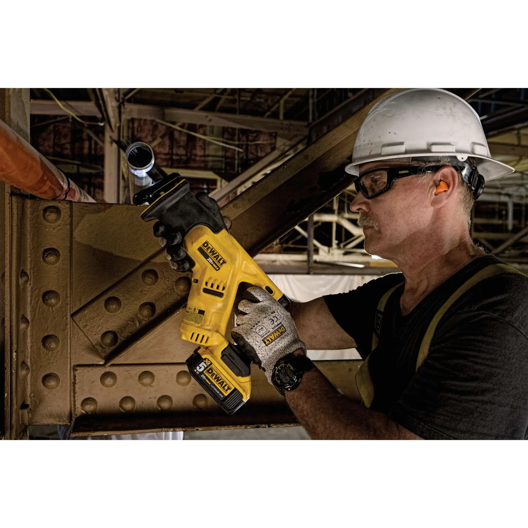 A person wearing a white helmet and gloves is using a DEWALT DCS387P1 cordless reciprocating saw to cut a metal pipe in an industrial setting. The person's face is blurred for privacy.
