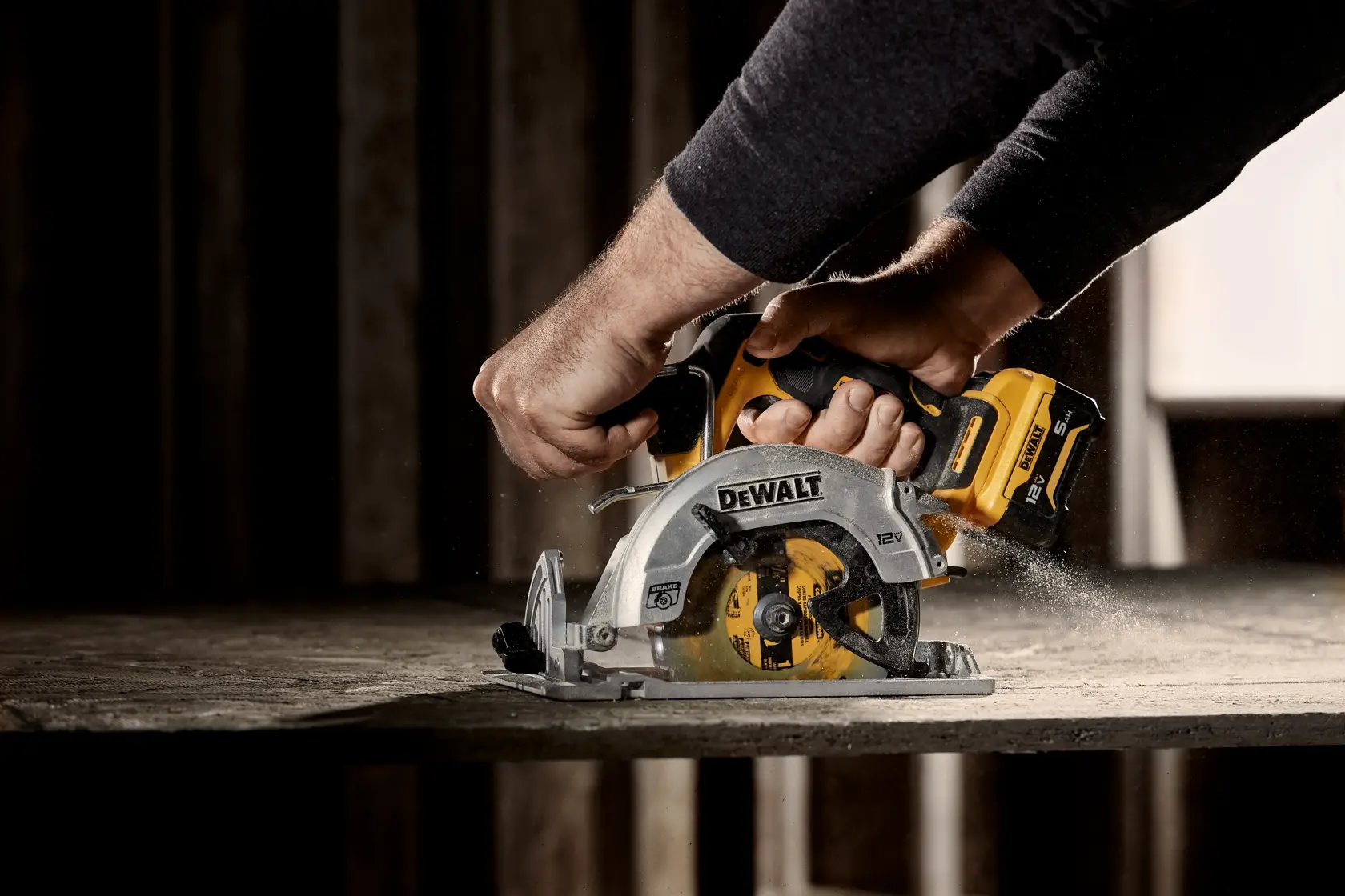 A close-up of hands operating a DEWALT cordless circular saw, cutting through a wooden surface, with sawdust visible.
