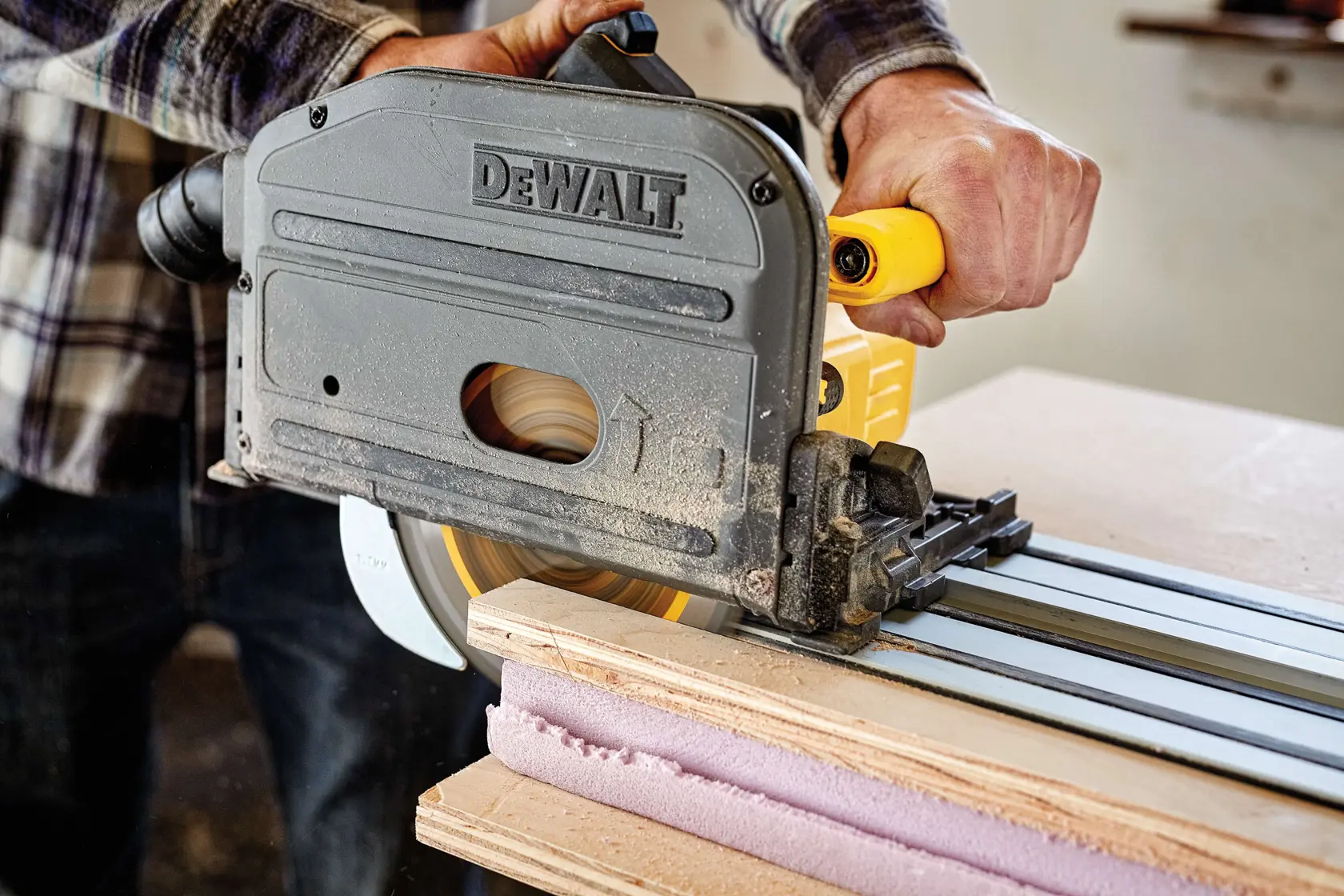 A person using a DEWALT track saw to cut wooden boards with a guide rail in a workshop.