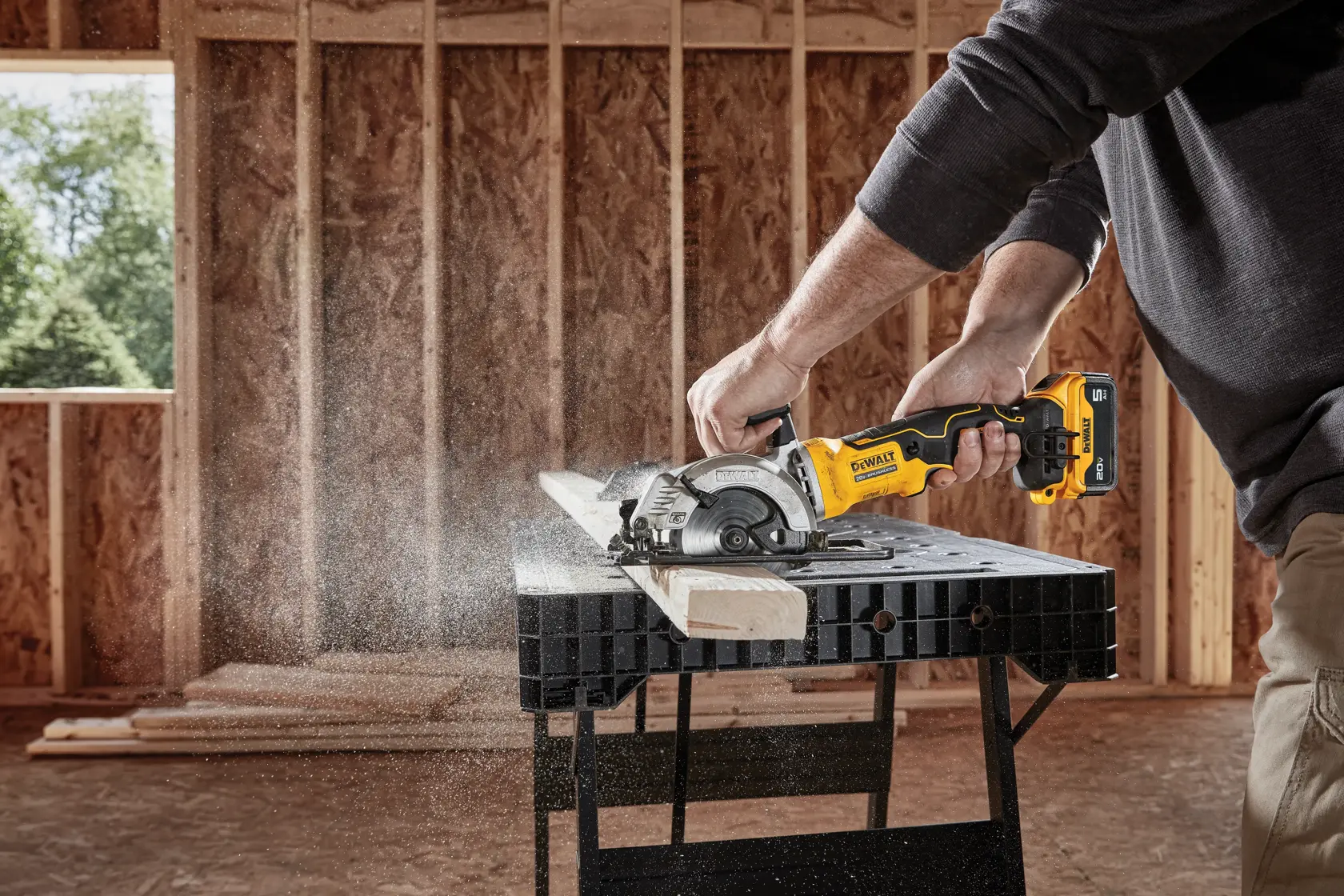 A person using a DEWALT DCS571B cordless circular saw to cut a piece of wood on a workbench in a construction site.