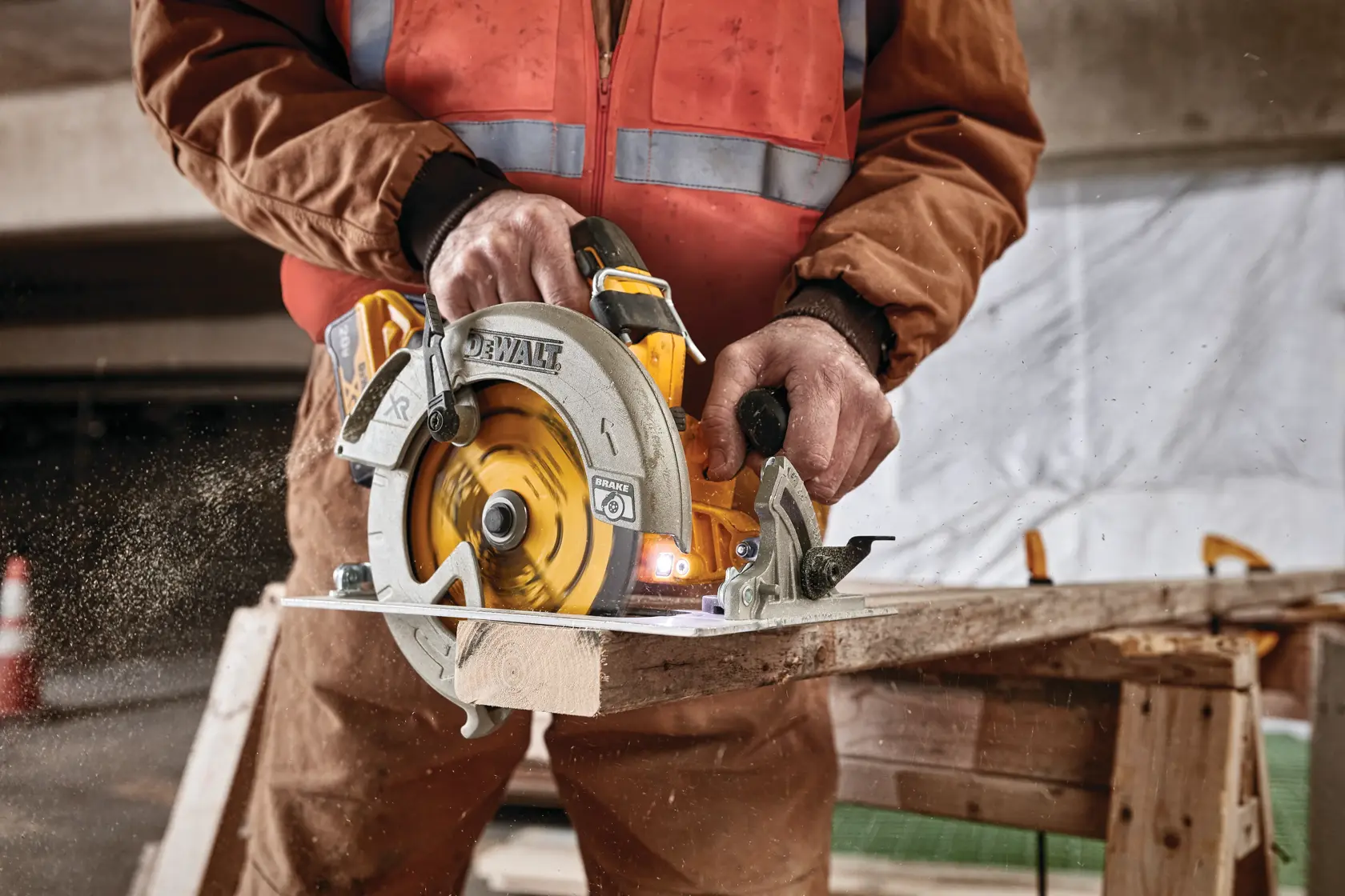 Une personne utilise une scie circulaire DEWALT pour couper une pièce de bois, avec de la sciure volante. La scène semble se dérouler sur un chantier, et la personne porte un gilet de sécurité et des vêtements de travail marron.