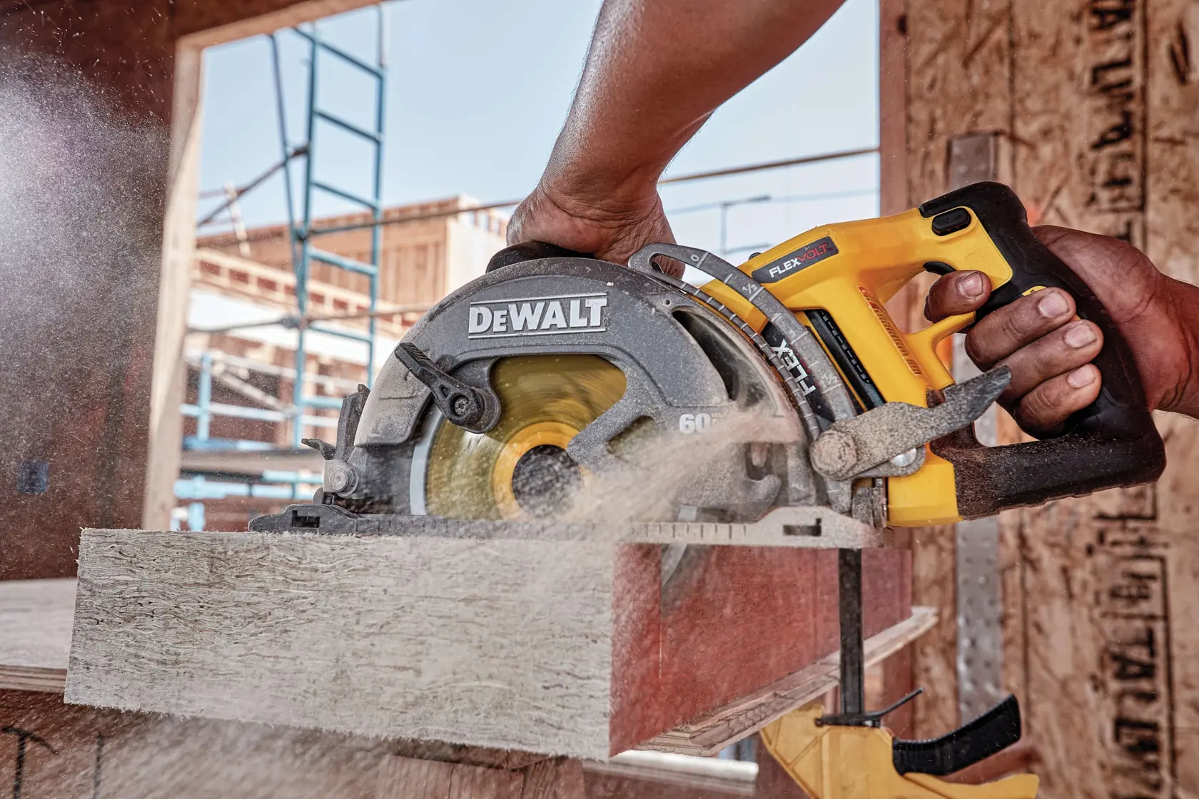 A close-up image of a DEWALT cordless circular saw being used to cut through a piece of wood, with sawdust flying. The saw is held by a person, and construction materials and scaffolding are visible in the background.