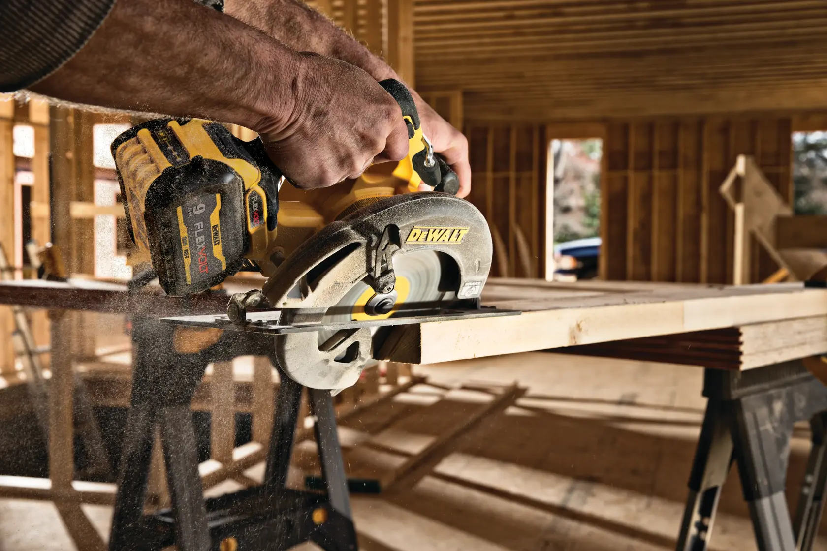 A person using a DEWALT DCS578X1 cordless circular saw to cut a wooden plank in an unfinished construction site.