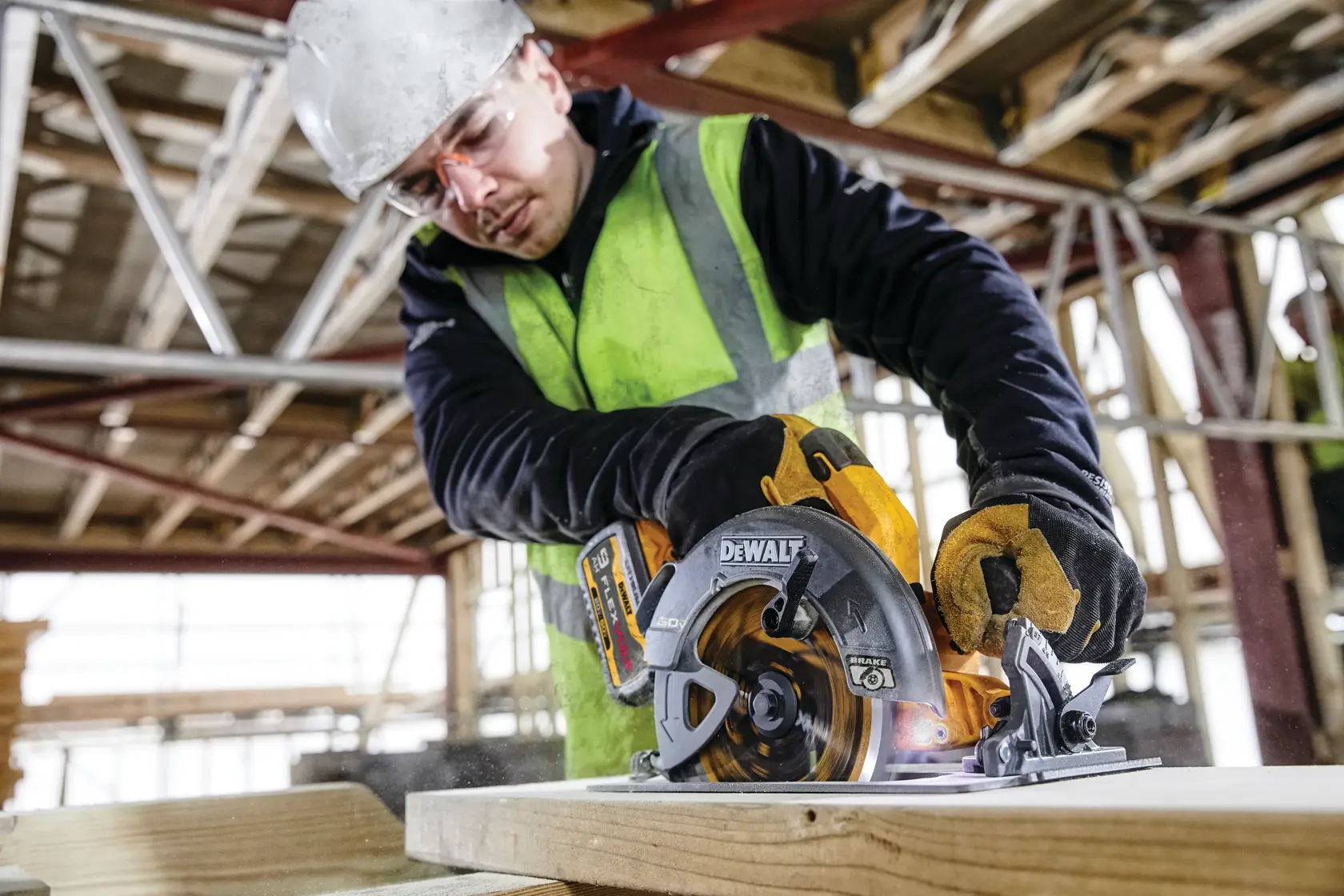 Person wearing gear operates DEWALT DCS578X2 circular saw to cut wood at a construction site.