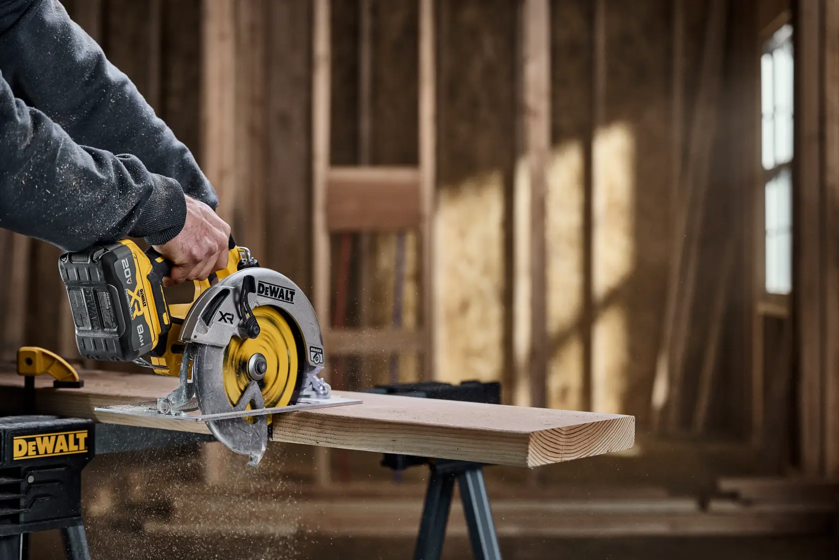 A DEWALT cordless circular saw is being used to cut a wooden plank, with sawdust flying. The saw is placed on a workbench inside a partially constructed wooden structure.