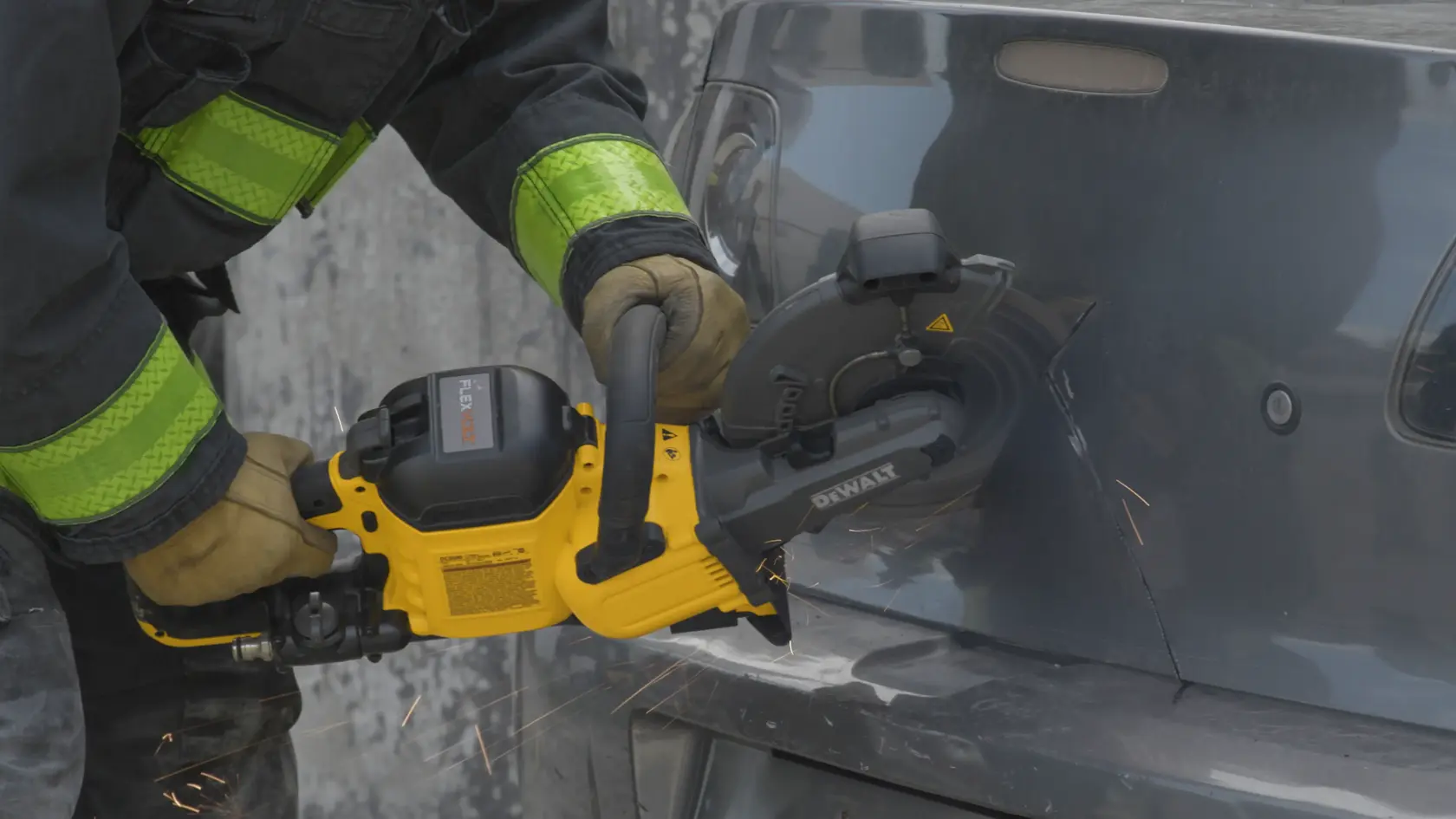 A person wearing protective gloves is using a yellow DEWALT cordless cut-off saw to cut through the metal body of a vehicle, producing sparks.