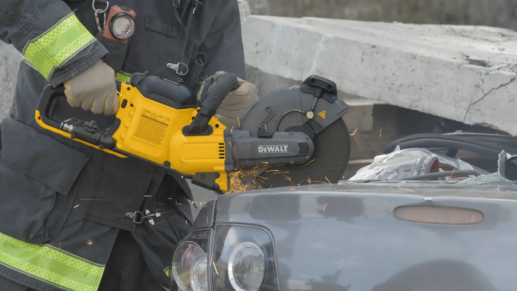 A person wearing protective clothing is using a yellow DEWALT DCS692B power saw to cut through the metal frame of a car, with sparks flying from the cutting area.