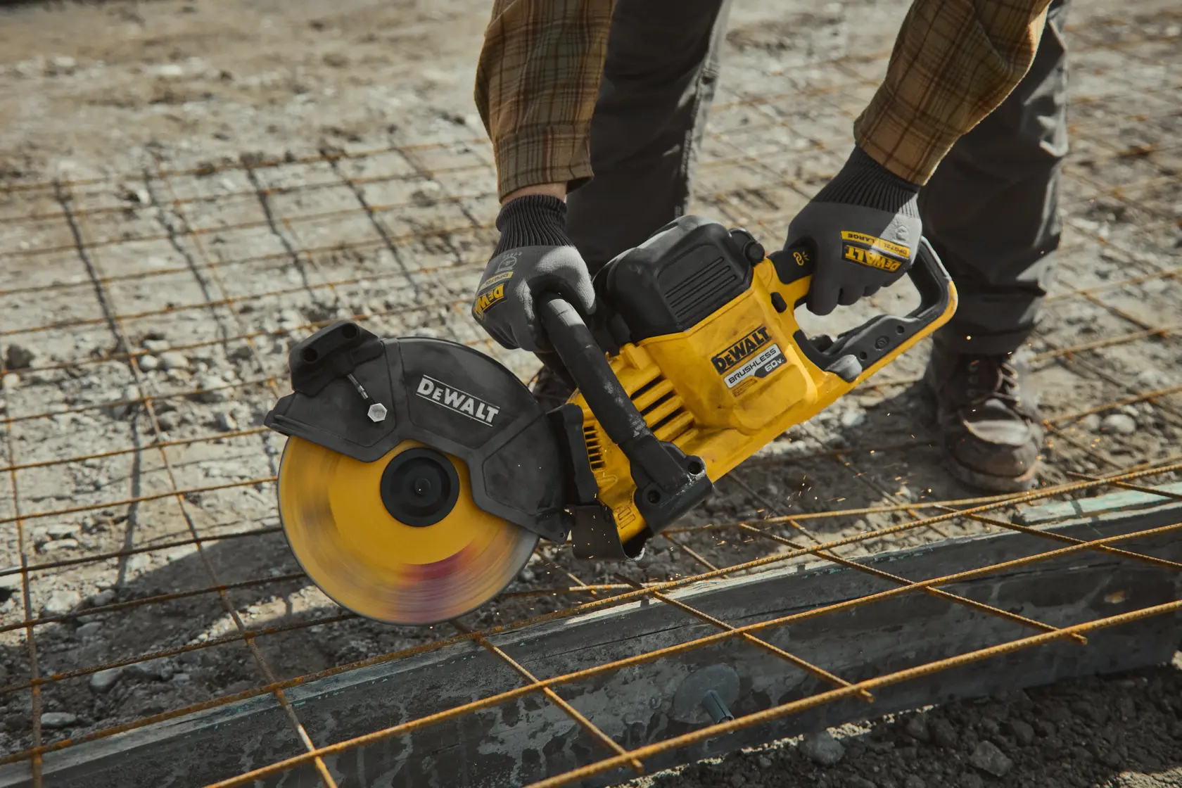 A person using a DEWALT DCS692X2 cordless cut-off saw to cut through metal rebar on a construction site. The saw is yellow and black and sparks are visible while cutting.