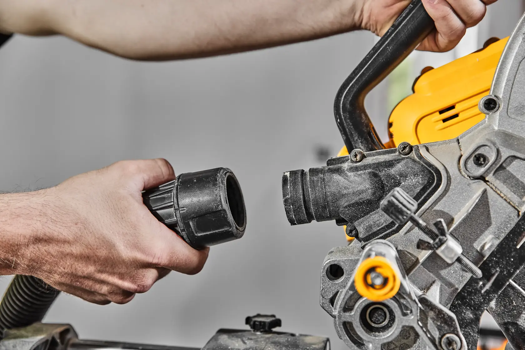 Close-up of a person attaching a dust extraction hose to a DEWALT miter saw.