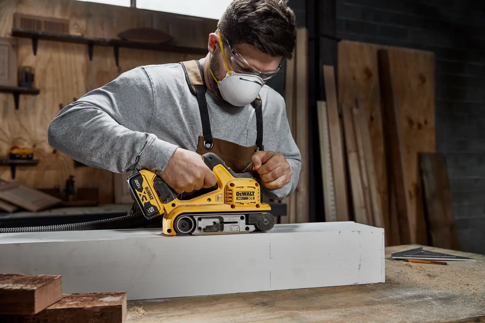 Close-up view of a DEWALT 20V XR brushless power tool, specifically a belt sander, showing a quick-release mechanism for easy sanding belt replacement. Text in French on the image highlights the quick band replacement and easy abrasive paper change features.
