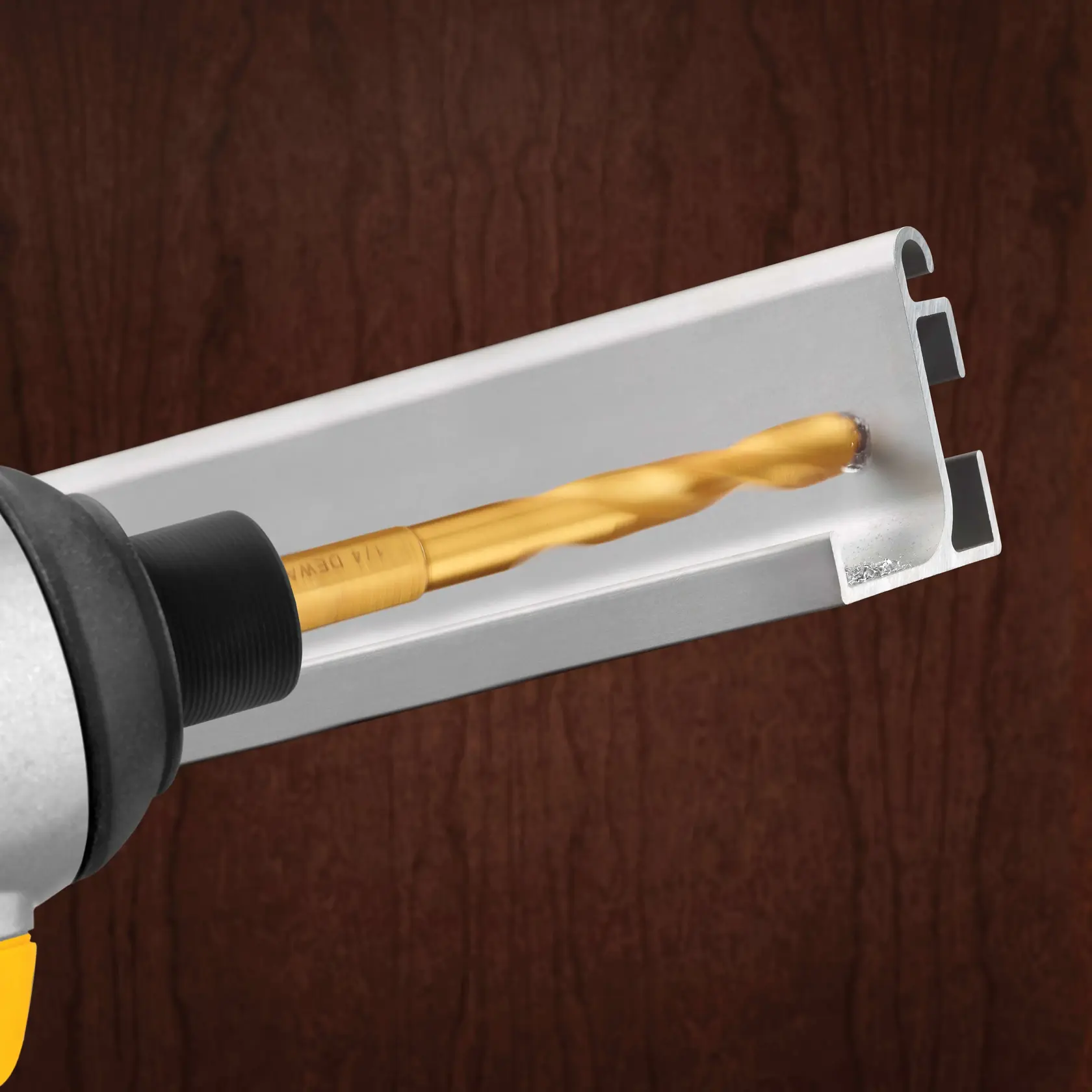 A close-up of a DEWALT drill bit drilling into a piece of metal, with a dark wooden background.