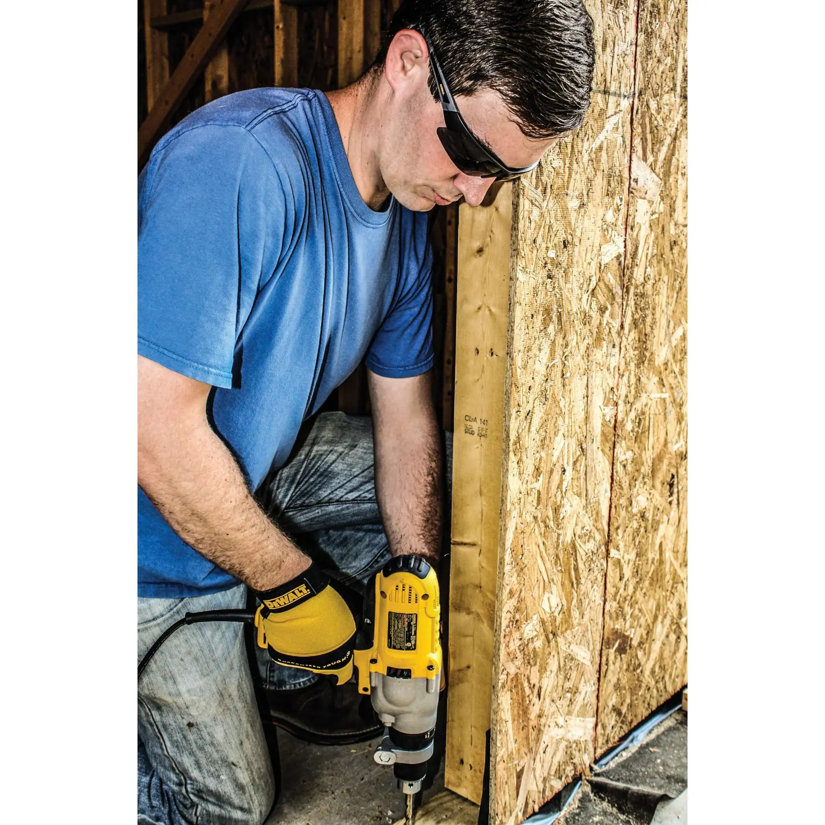 A person wearing a blue shirt and yellow DEWALT-branded gloves is using a DEWALT power drill to work on a wooden structure, likely for construction purposes.