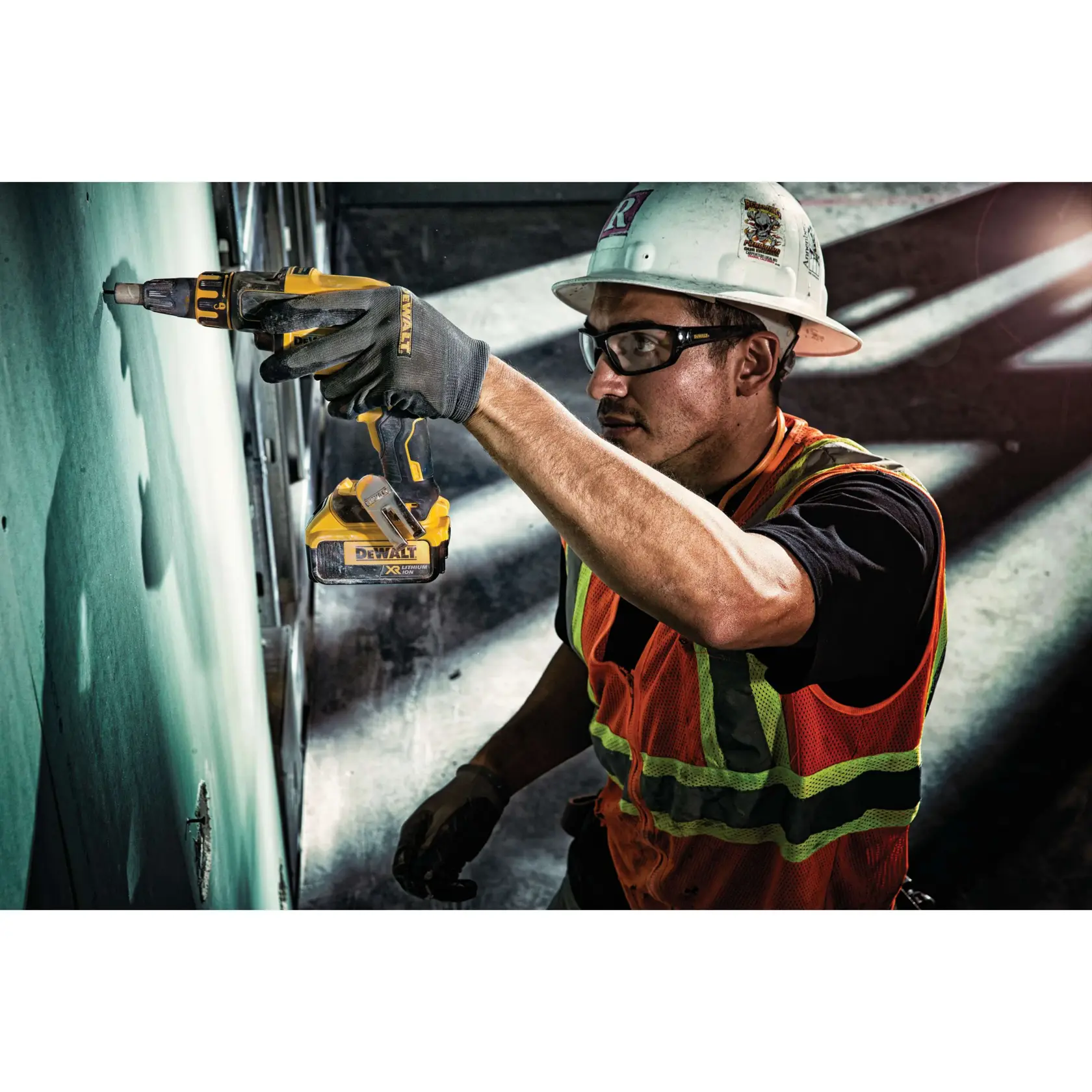 A construction worker wearing a hard hat, safety vest, and gloves is using a DEWALT cordless power tool to drill or screw into a wall on a work site.