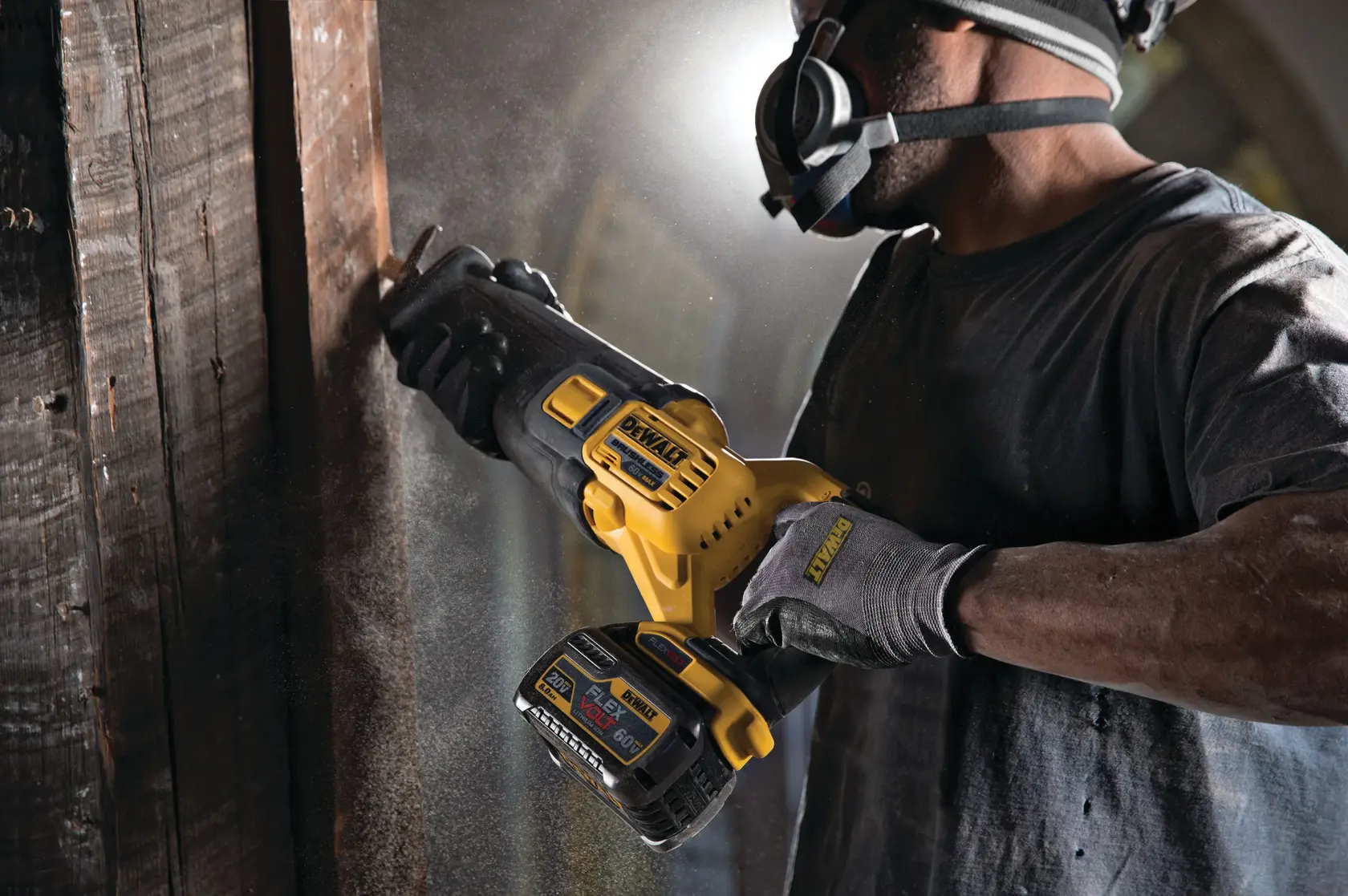A person wearing protective gear uses a DEWALT cordless reciprocating saw to cut through wooden beams. Dust is visible in the air, and the DEWALT branding is seen on the tool and gloves.
