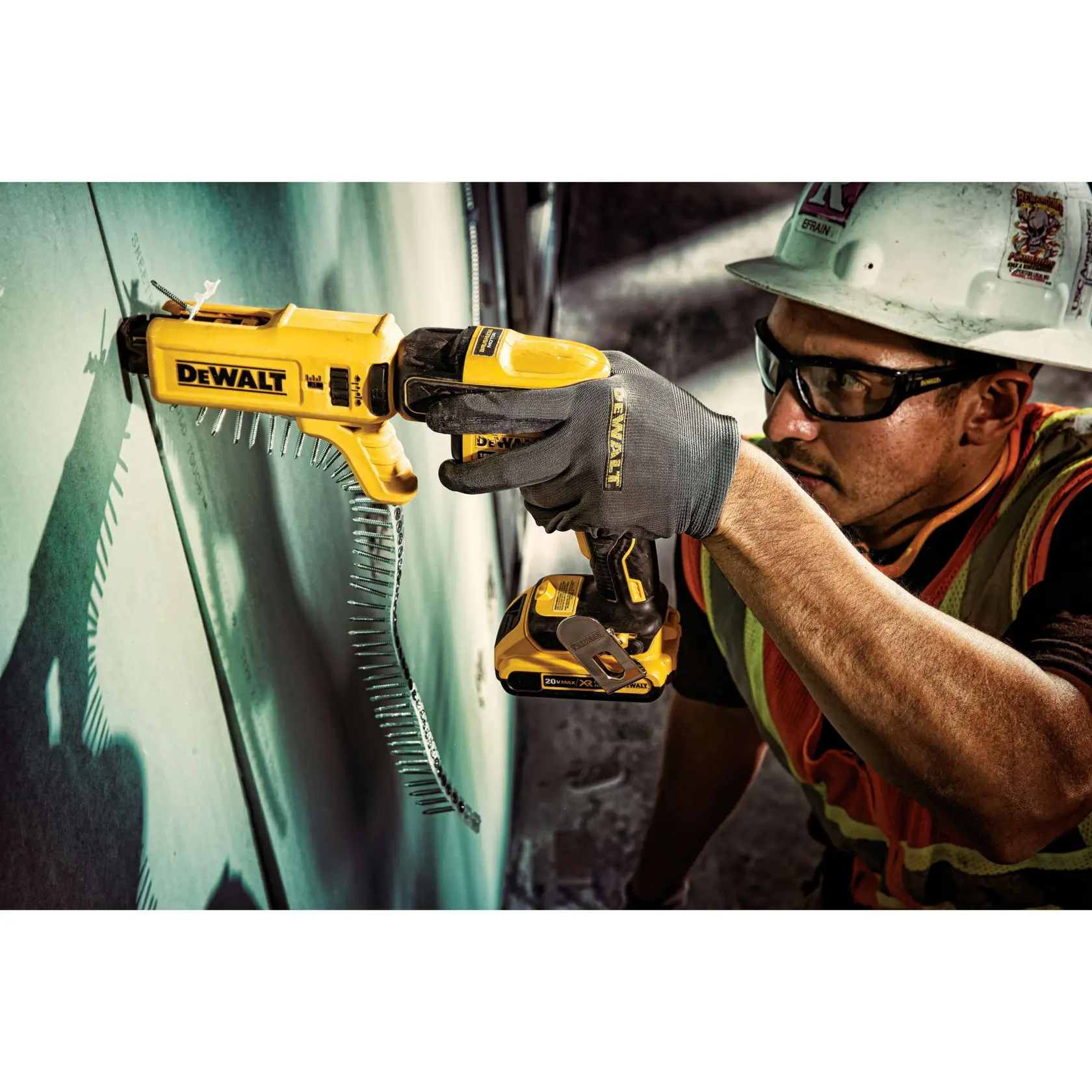 A worker using a yellow DEWALT automatic screw gun to attach drywall screws to a wall. The worker is wearing gloves, a safety vest, and a hard hat. The DEWALT tool is shown in action with a strip of screws feeding into it.