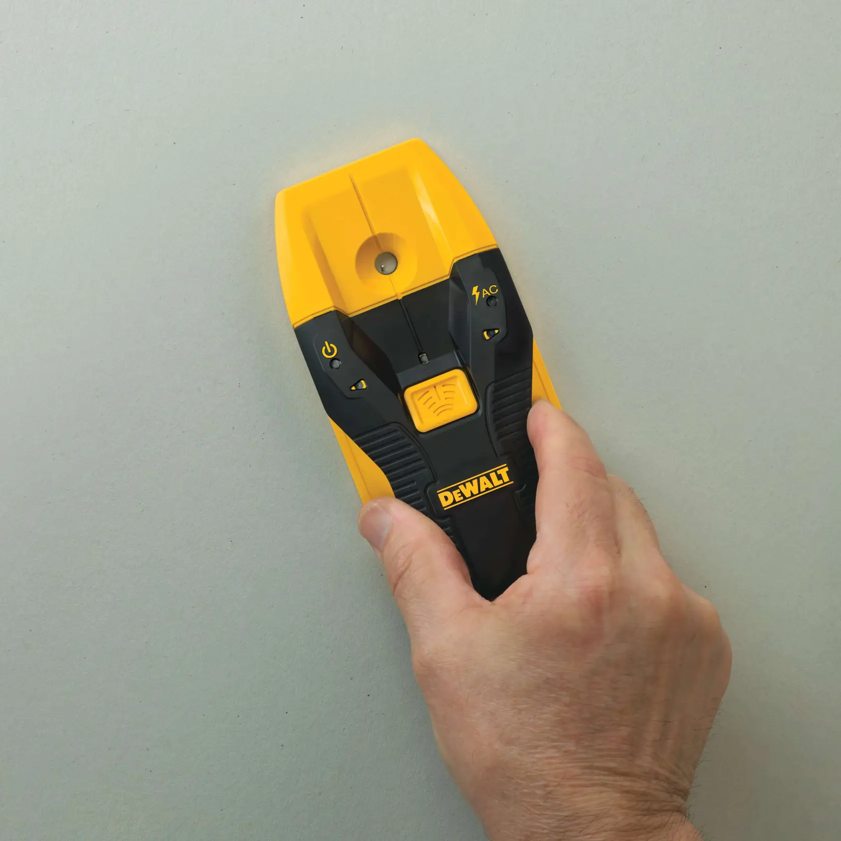 A hand holding a DEWALT electronic wall scanner with yellow and black casing, used for detecting studs and wires inside walls.