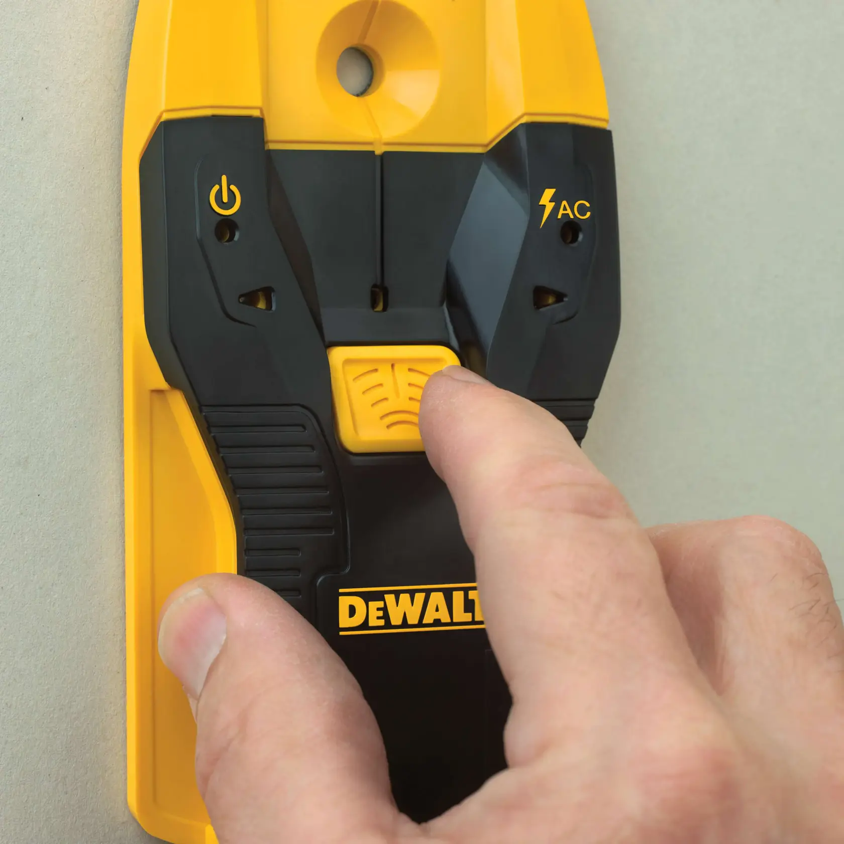 Close-up of a person's hand pressing a button on a DEWALT electronic stud finder against a wall.
