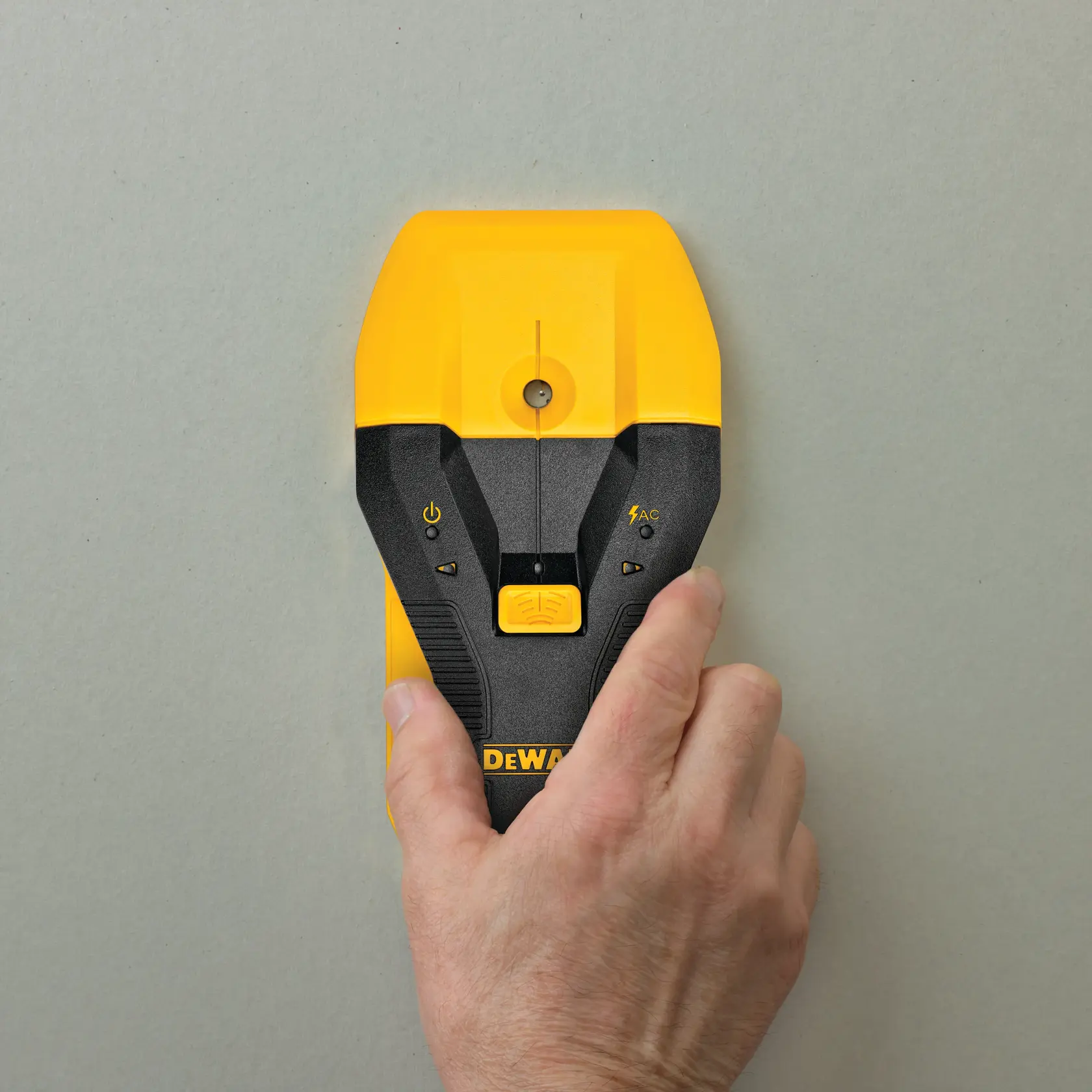 A hand holding a DEWALT stud finder, model DW0150, against a gray wall.