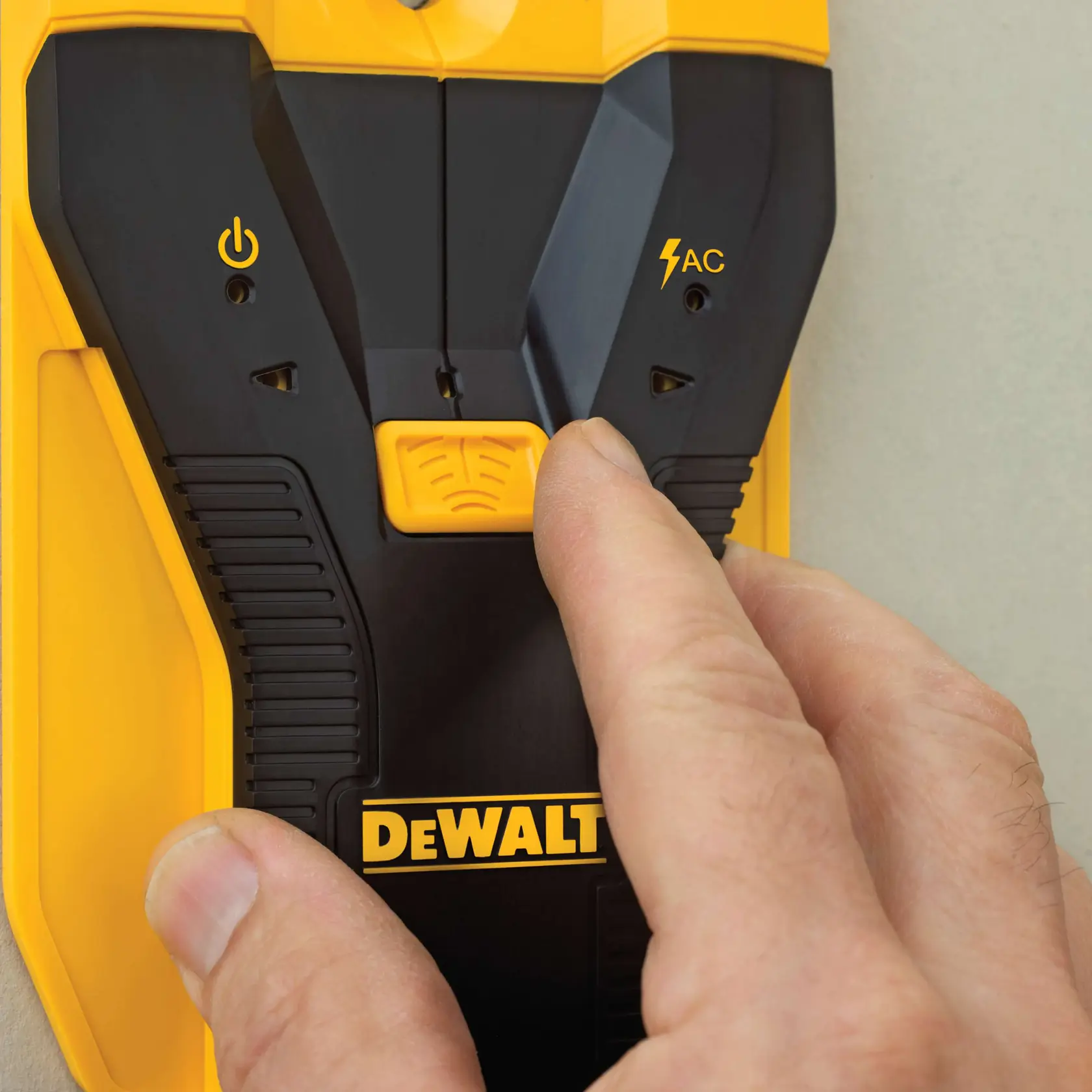A close-up of a hand operating a DEWALT electronic wall scanner, showing the brand logo and control buttons on the device.