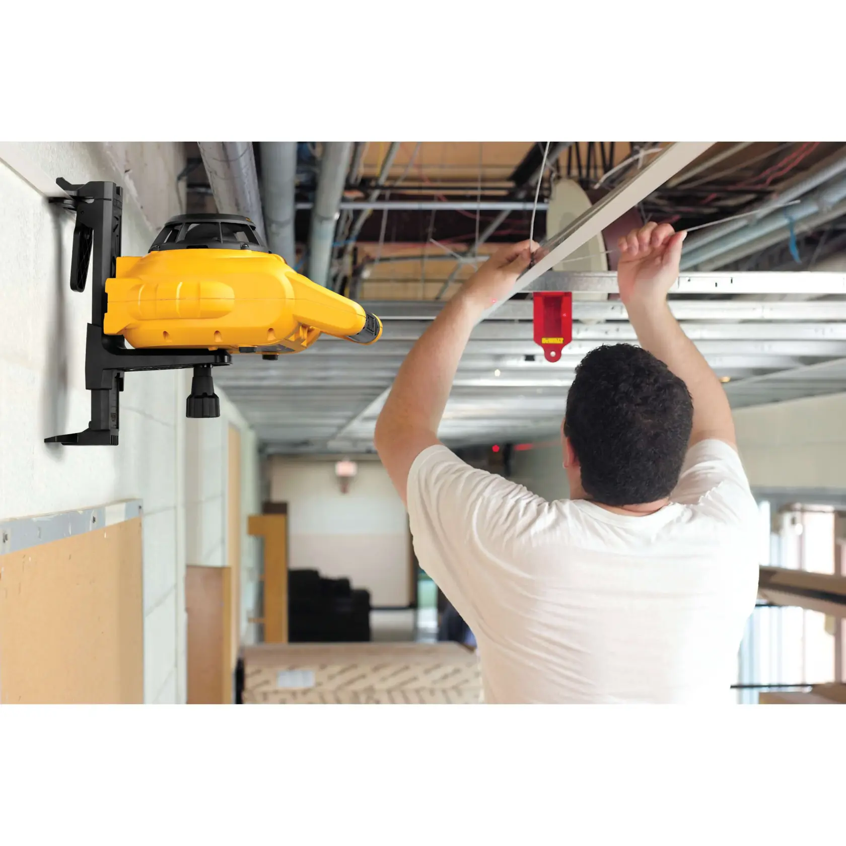 A person is adjusting metal framing on a ceiling while using a mounted yellow DEWALT laser level device for alignment in a construction setting.