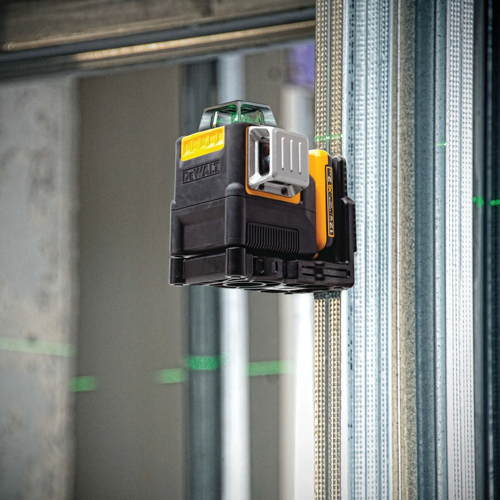A DEWALT green laser level device (model DW0811LG) mounted on a metal stud in a construction setting, projecting visible green laser lines horizontally and vertically for alignment purposes.