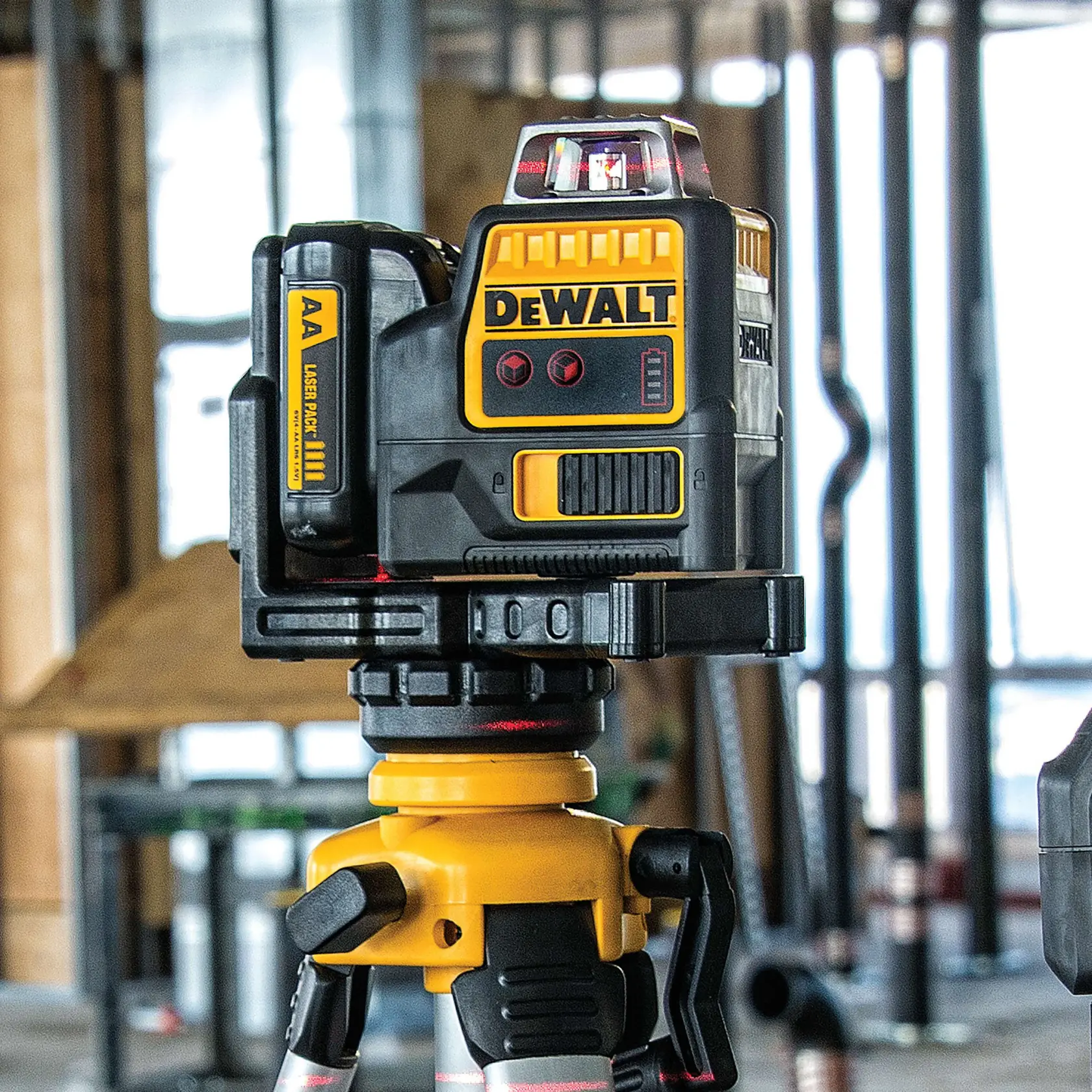 A DEWALT DW0811LR laser level device mounted on a tripod, shown in an industrial setting with construction materials in the background.