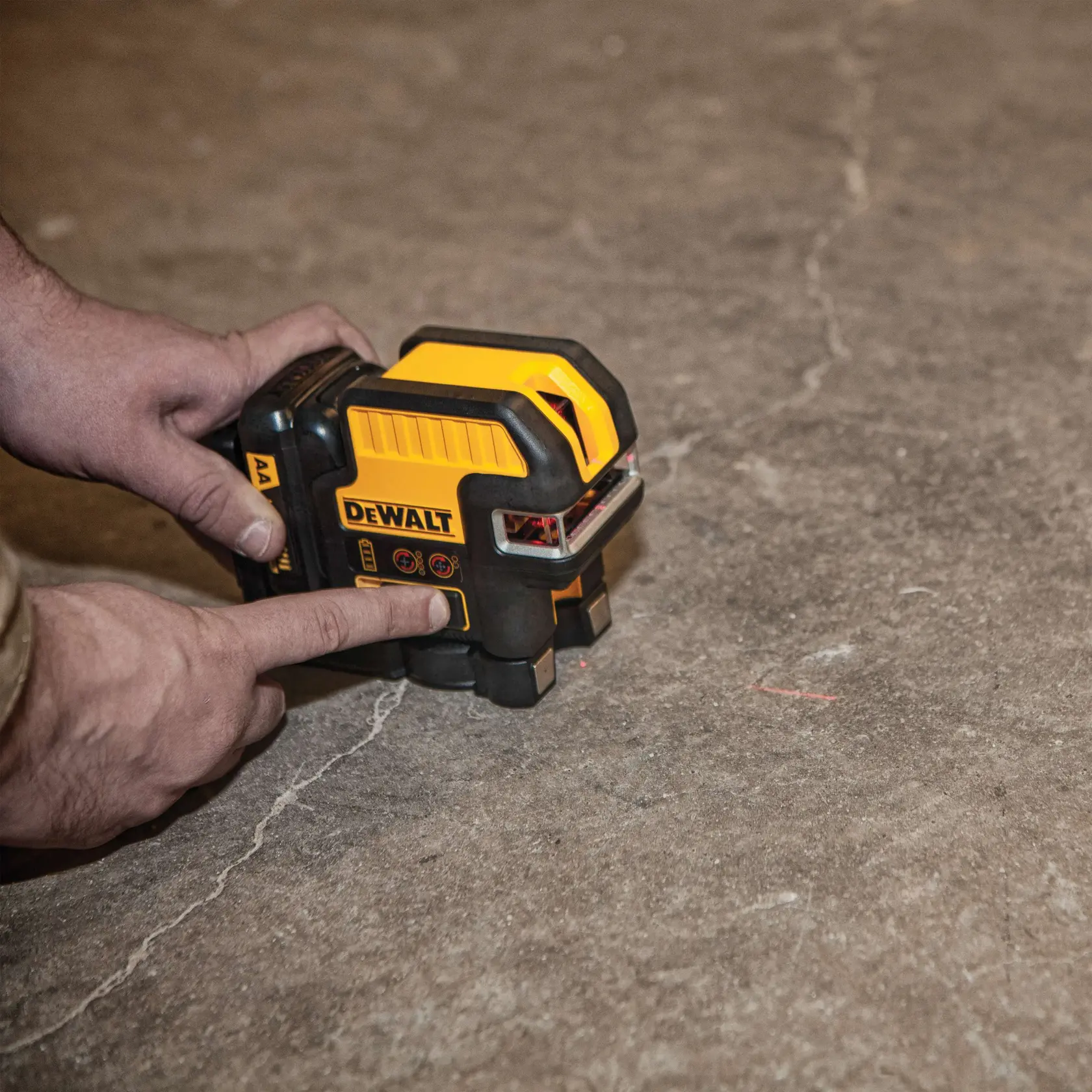 A person operating a DEWALT laser level device on a concrete floor. The device is yellow and black, with visible control buttons and a DEWALT logo, used for precise alignment in photography or construction.