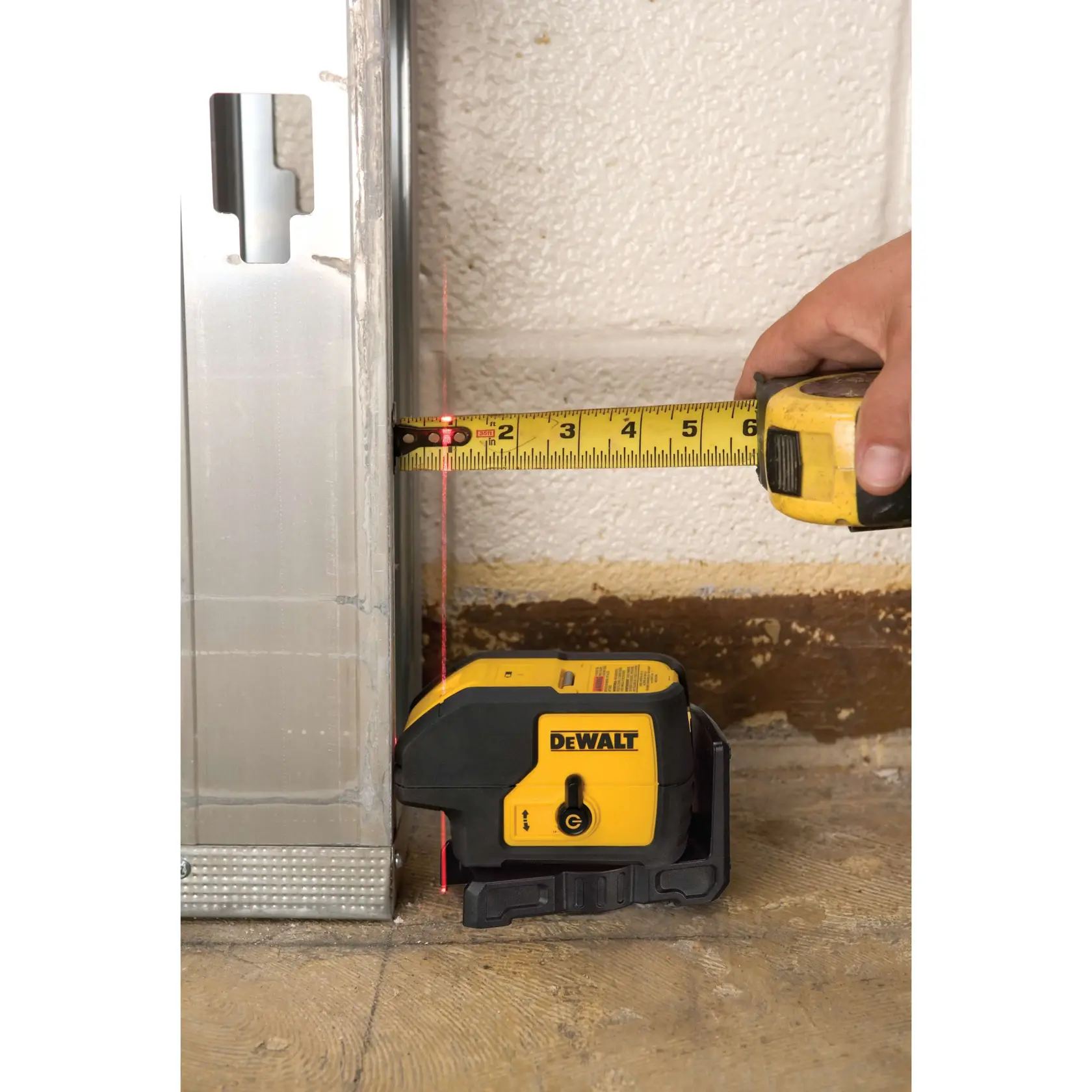 DEWALT laser level aligns metal frame with wall, tape measure shows precise distance.