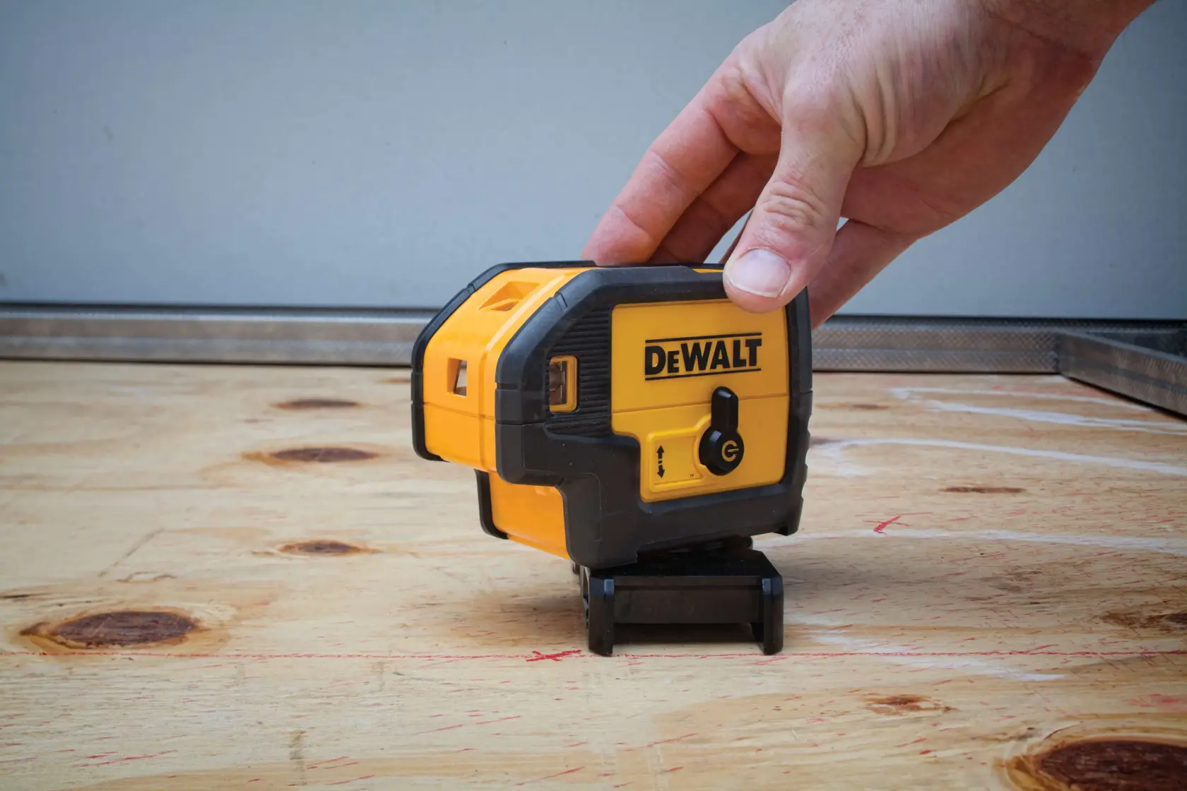 A DEWALT laser level device is being placed on a wooden surface by a hand. The device is yellow and black and has the DEWALT logo on it.
