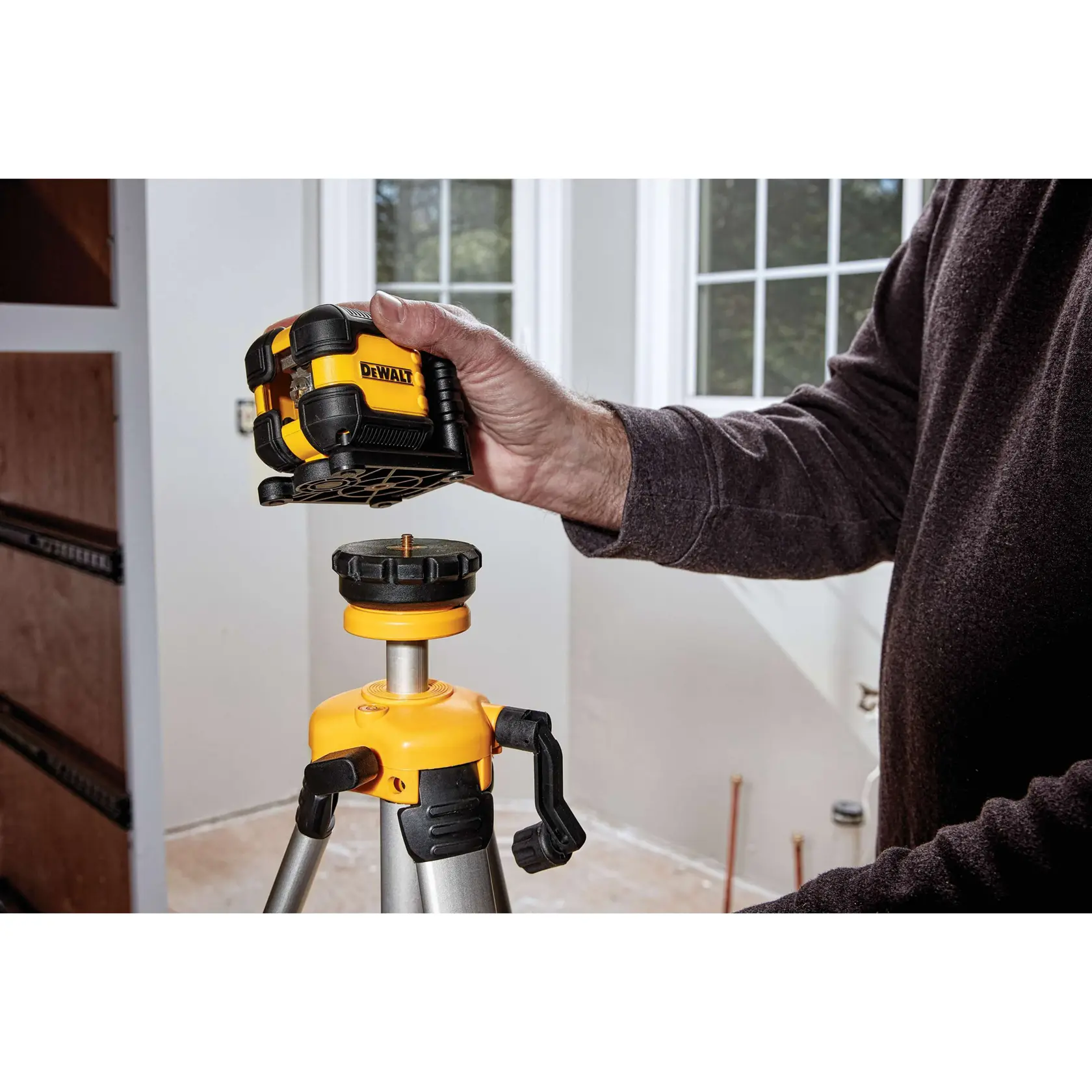 A DEWALT red cross line laser level kit is shown opened, displaying the yellow and black laser level device, two AA batteries, a ceiling bracket, and a black blow mold carrying case. Above the case, a list of included items is visible.