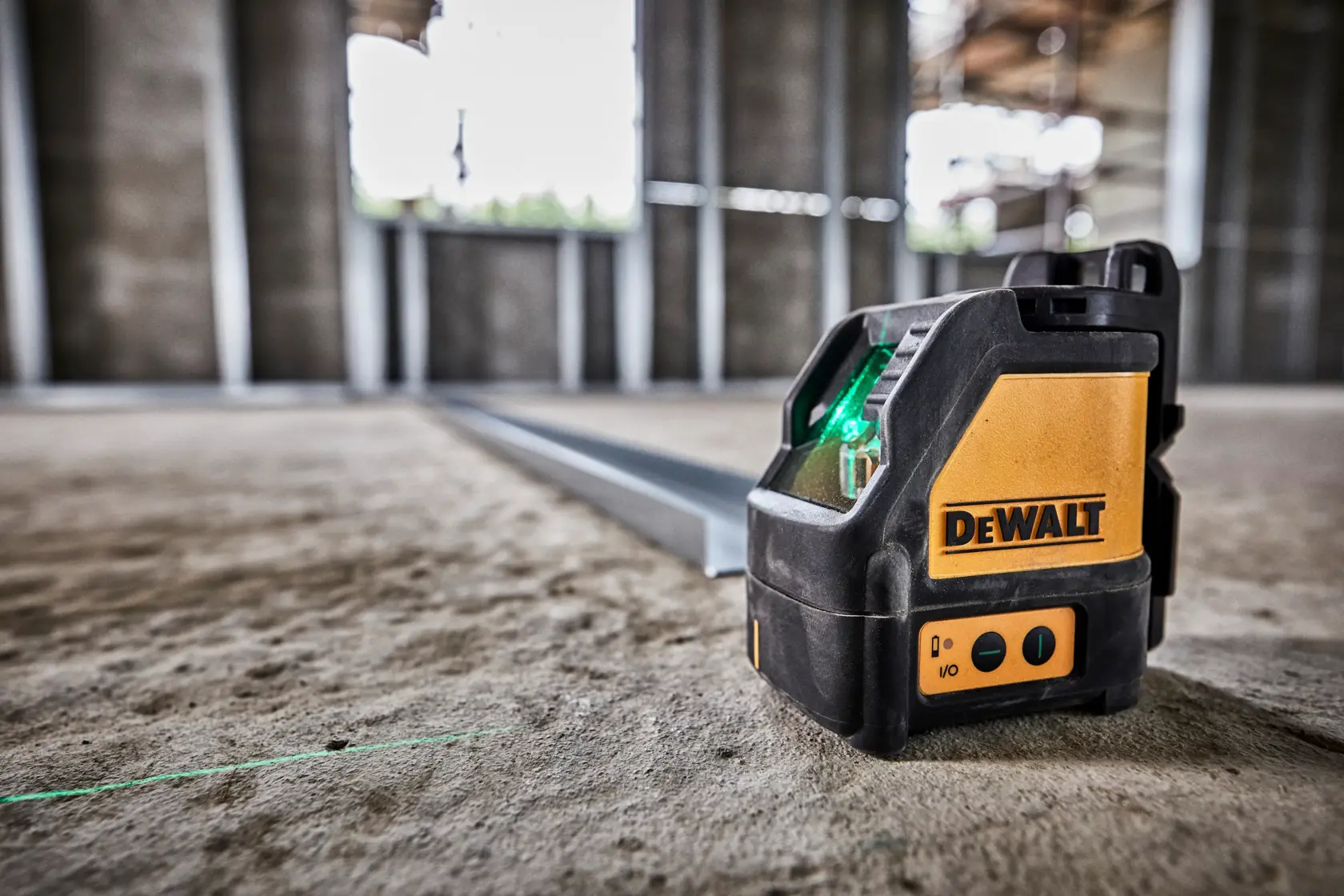 DEWALT green laser level DW088CG on a concrete floor inside a construction site, projecting a straight green line.