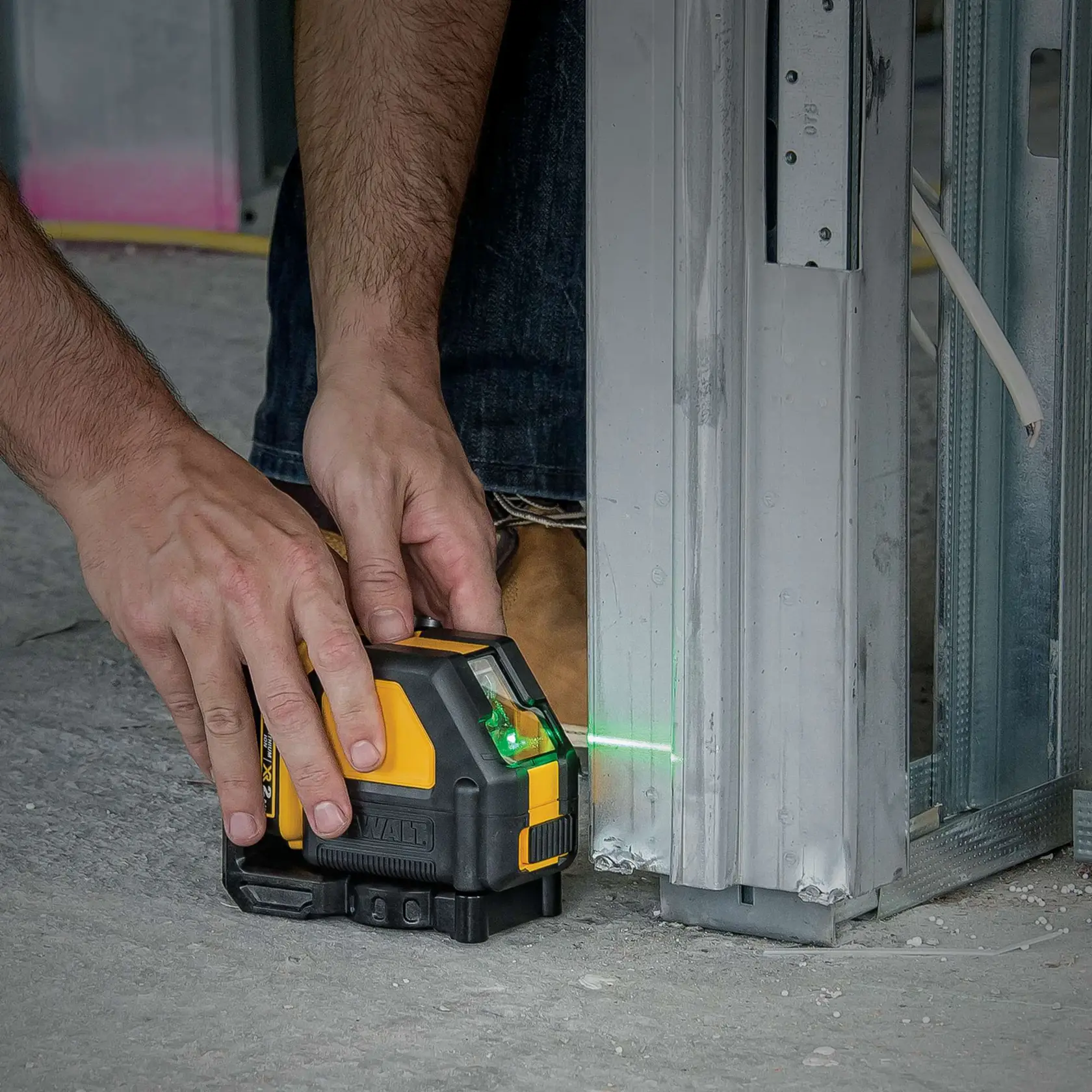 Close-up of a person using a DEWALT DW088LG green beam laser level to align a metal frame during construction work.