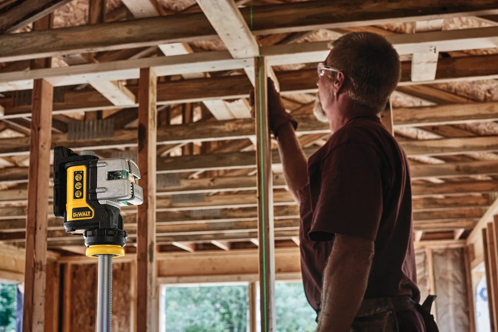 A DEWALT DW089CG green line laser level mounted on a tripod is shown in a room. A person is installing cabinetry, using the laser to align measurements precisely. The text at the bottom reads: 'Precise Alignment with the Micro Adjust Knob.'