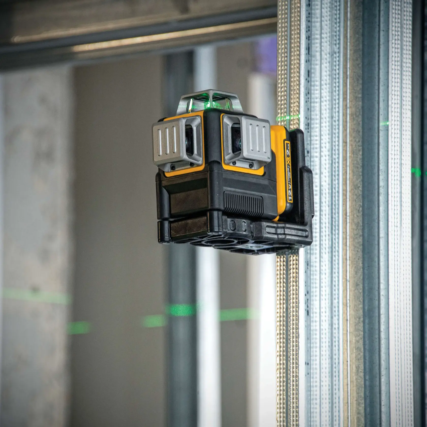 A DEWALT DW089LG green beam line laser level mounted on a steel framing stud in a construction setting, emitting green laser lines for precise alignment.