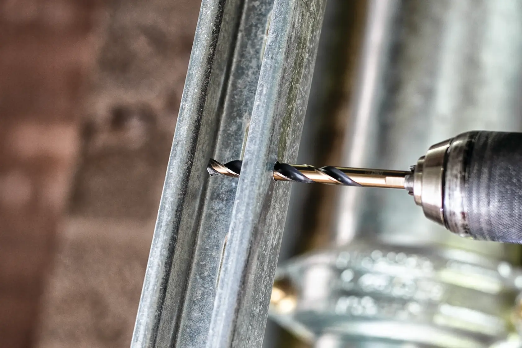 A close-up of a DEWALT drill bit attached to a power drill, drilling through a piece of metal.
