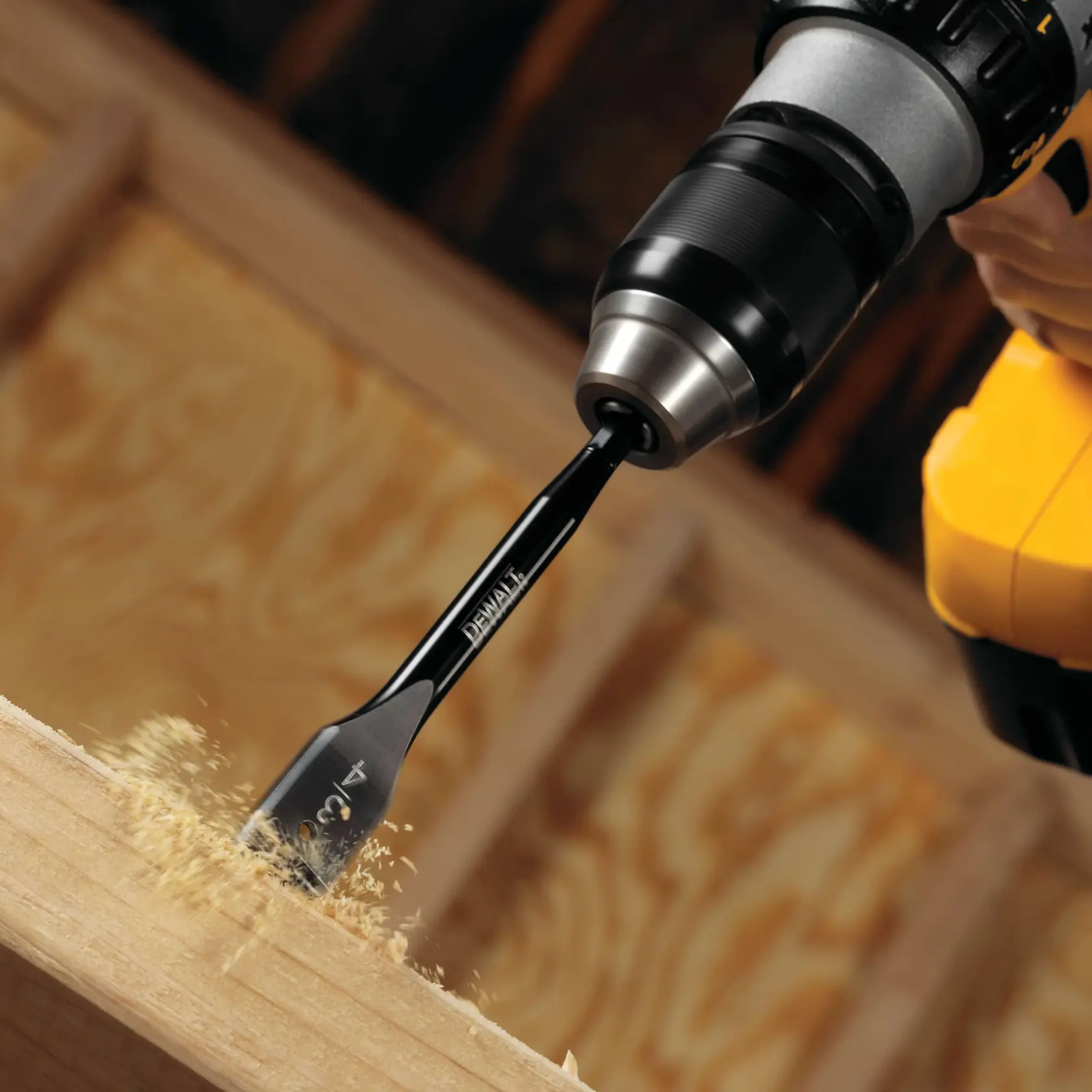 A DEWALT power drill with a flat spade bit drilling into a piece of wood, creating wood shavings.