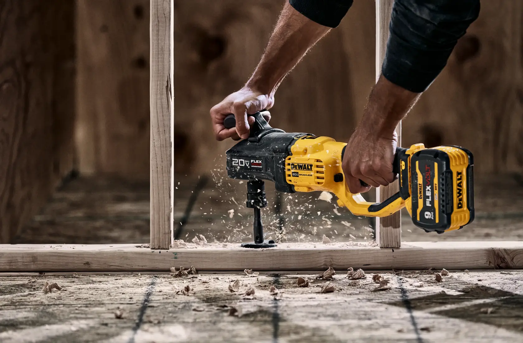 A person is using a DEWALT 20V cordless drill to bore a hole through a wooden plank, with wood shavings flying around during the drilling process.