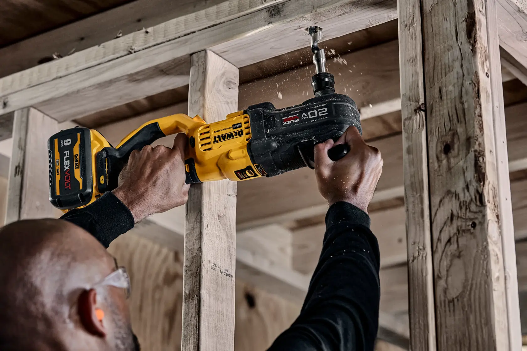 A person is using a DEWALT 20V cordless power drill with FLEXVOLT battery to drill into a wooden beam in a construction setting.