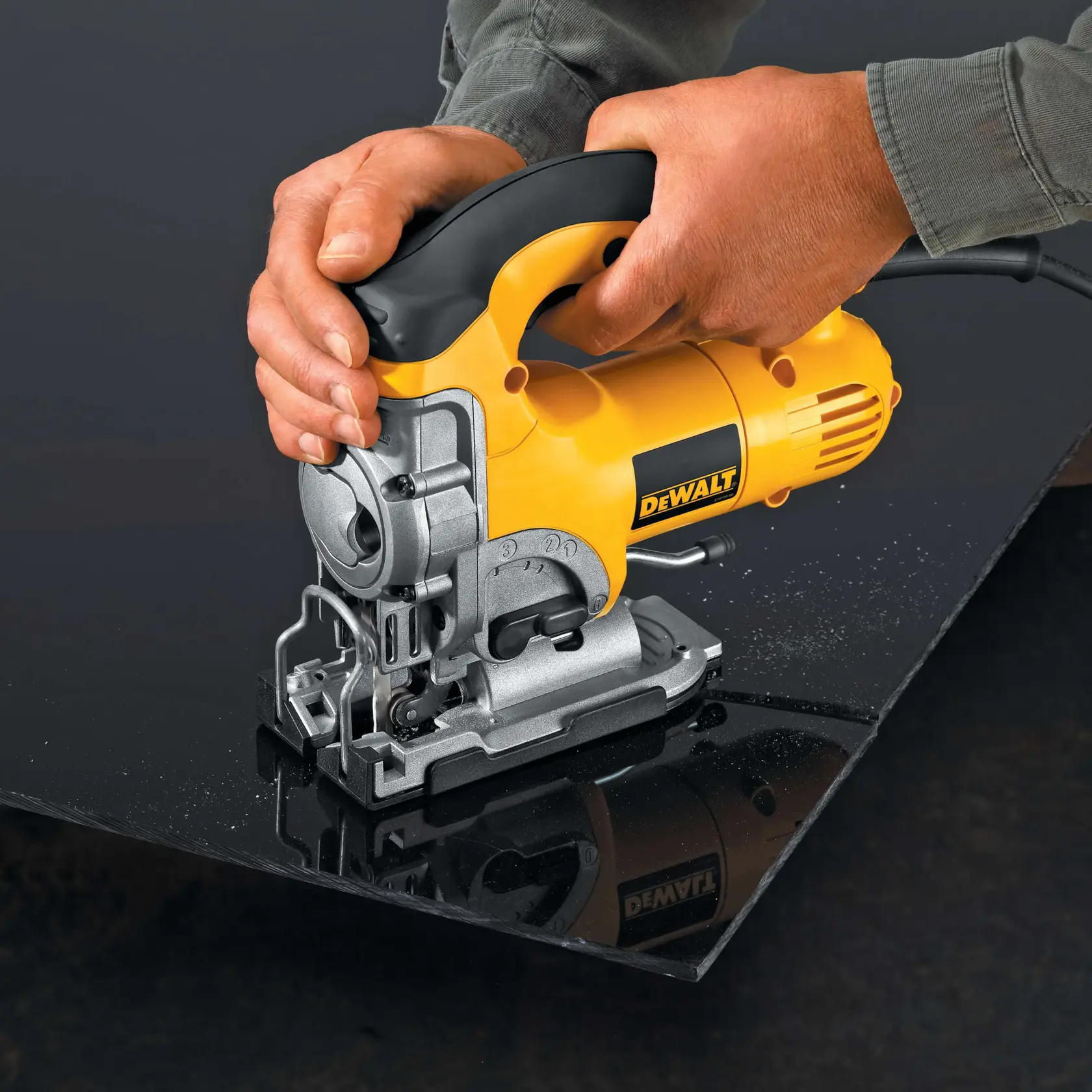 Hands operating a yellow DEWALT electric jigsaw on a dark sheet of material, cutting along an edge.