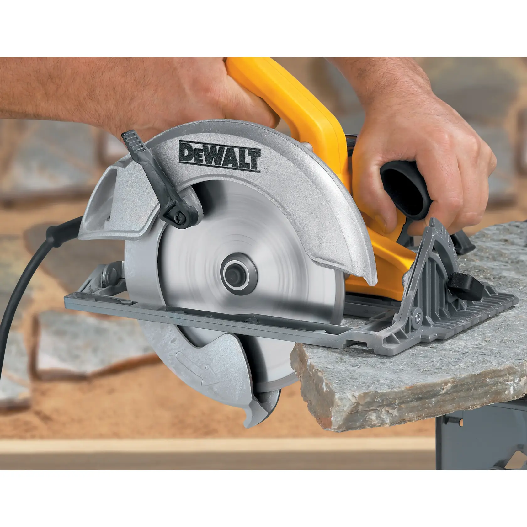 A person uses a DEWALT circular saw to cut through a piece of stone. The saw is plugged in and the blade is spinning, with hands firmly holding the tool for control.