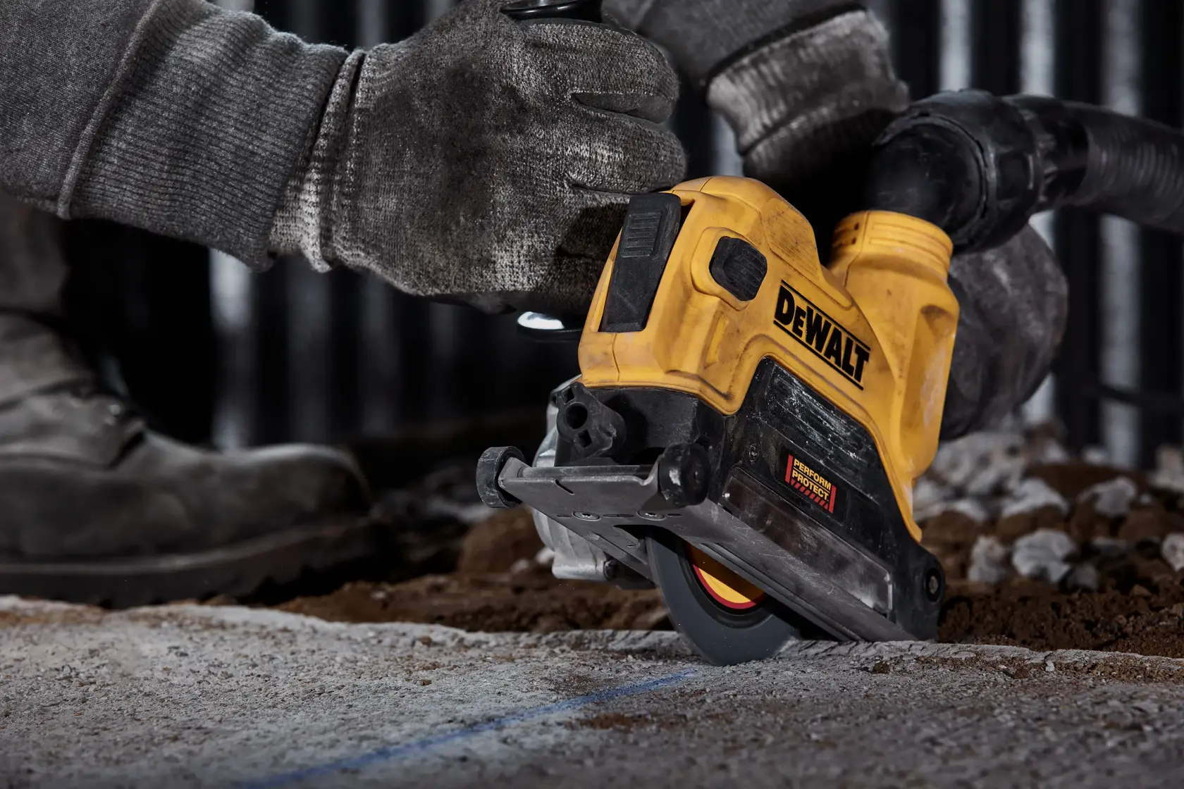 A person wearing gloves operates a DEWALT handheld power tool to cut concrete or stone, with a vacuum attachment for dust control.