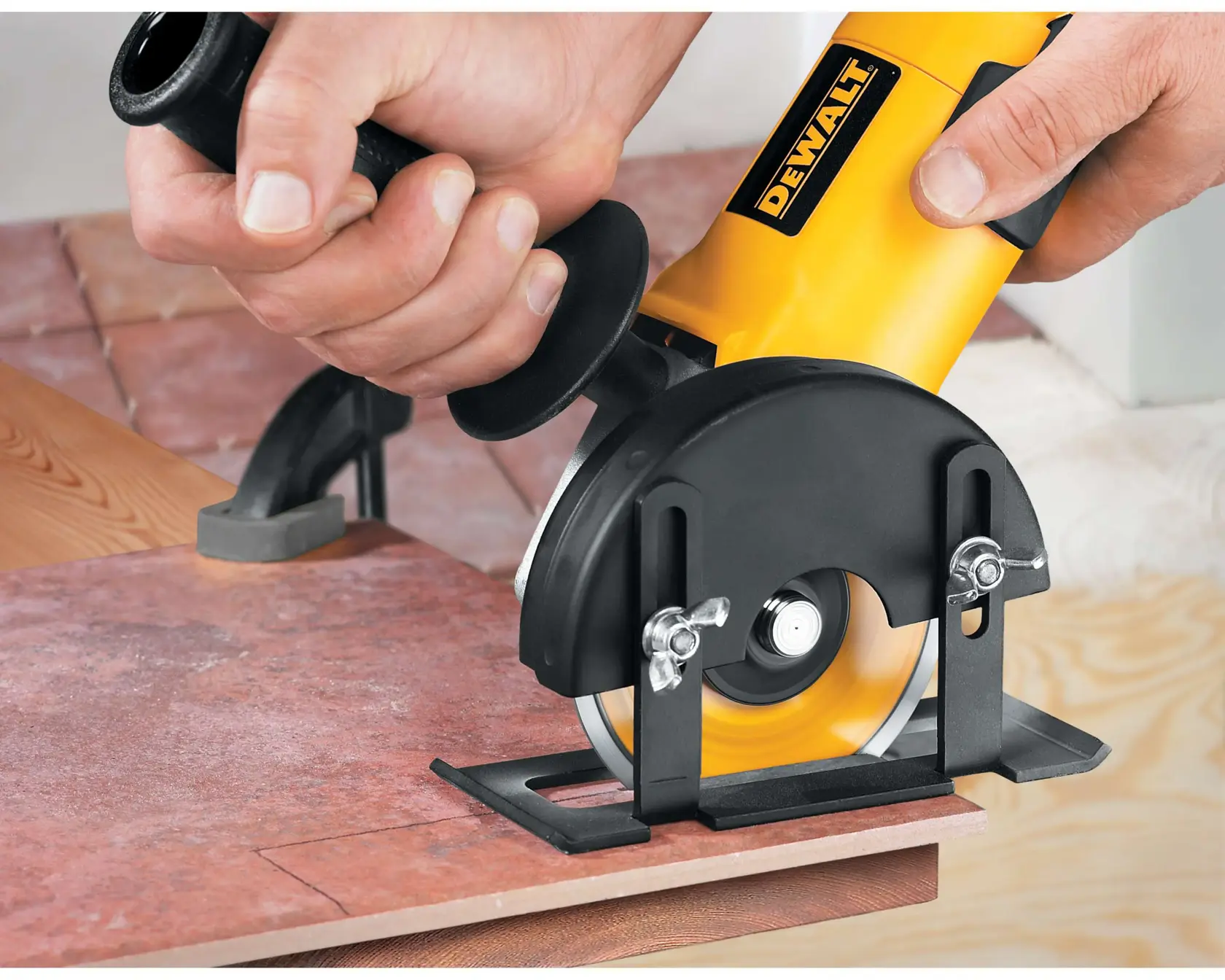 A close-up of a DeWalt power tool being used to cut a tile, showing hands gripping the tool and the blade in action.