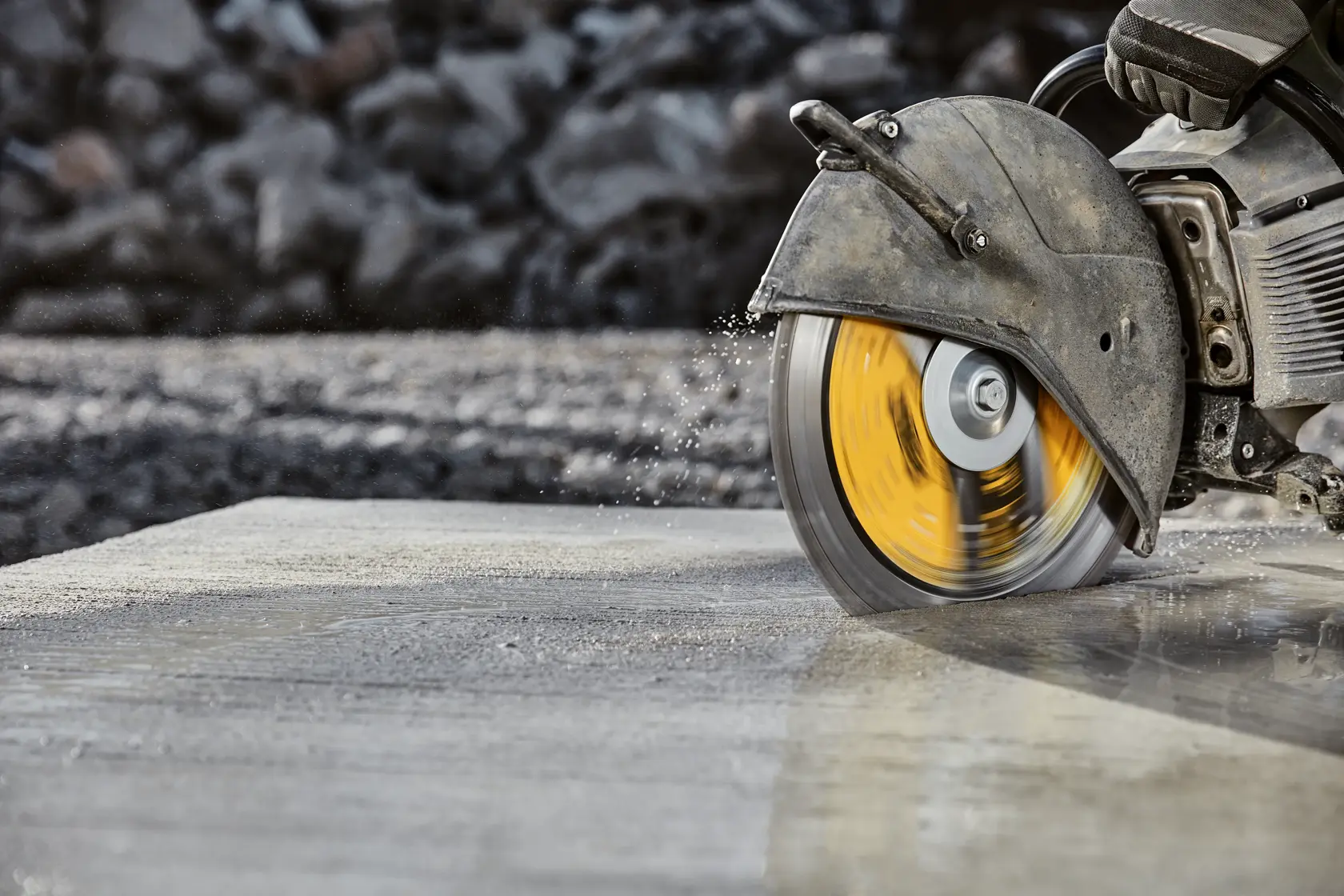 A close-up of a DEWALT power saw cutting through a concrete slab, with water spraying from the cutting area.