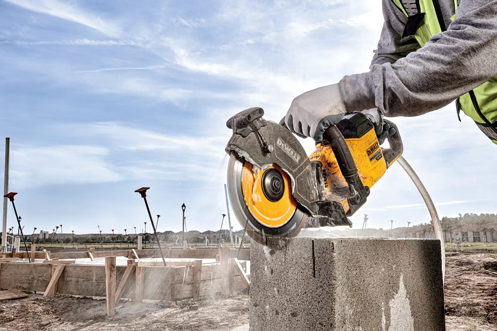 A person wearing gloves uses a DEWALT power tool to cut a concrete block at a construction site.